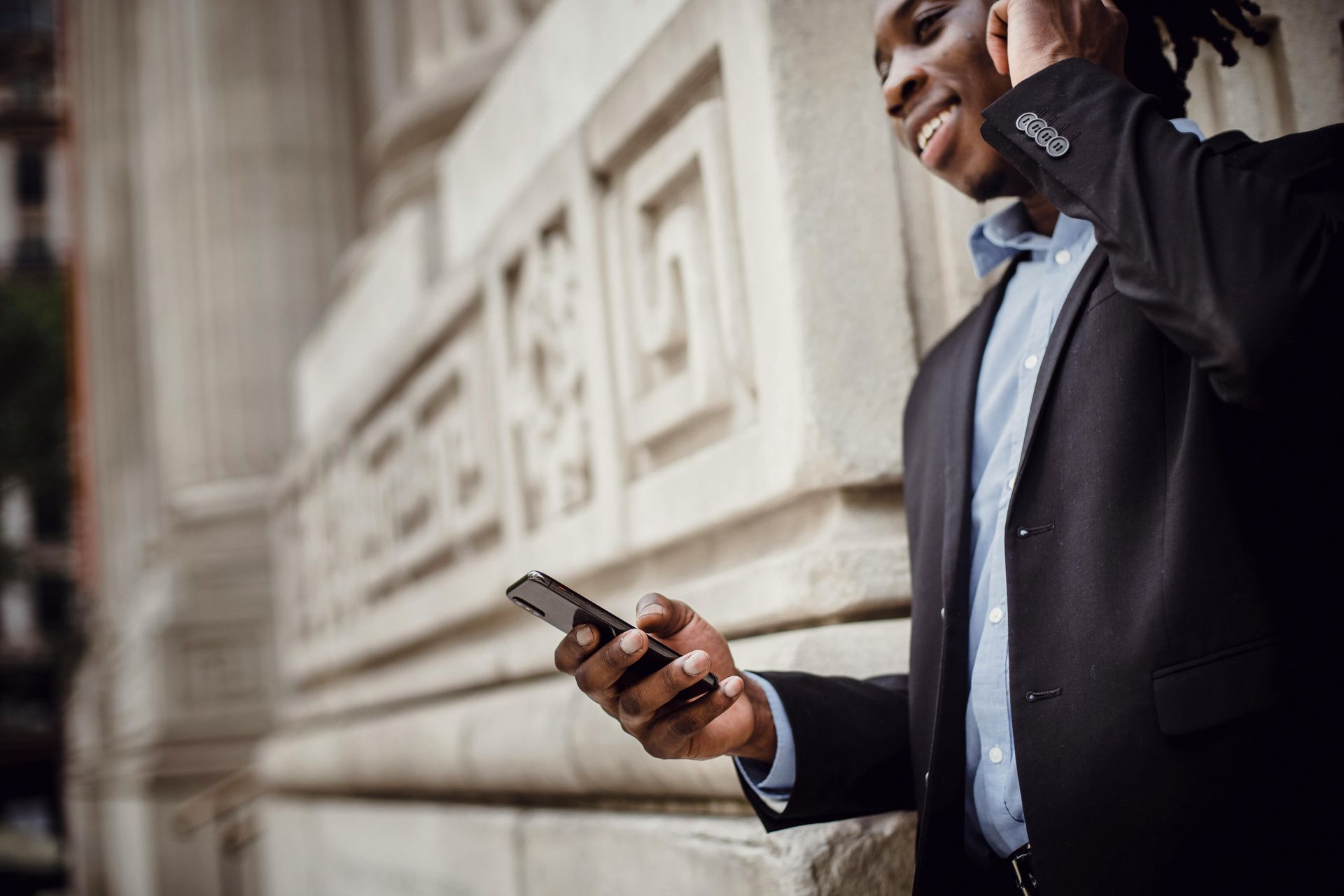 A man in a suit is talking on a cell phone while standing next to a building.