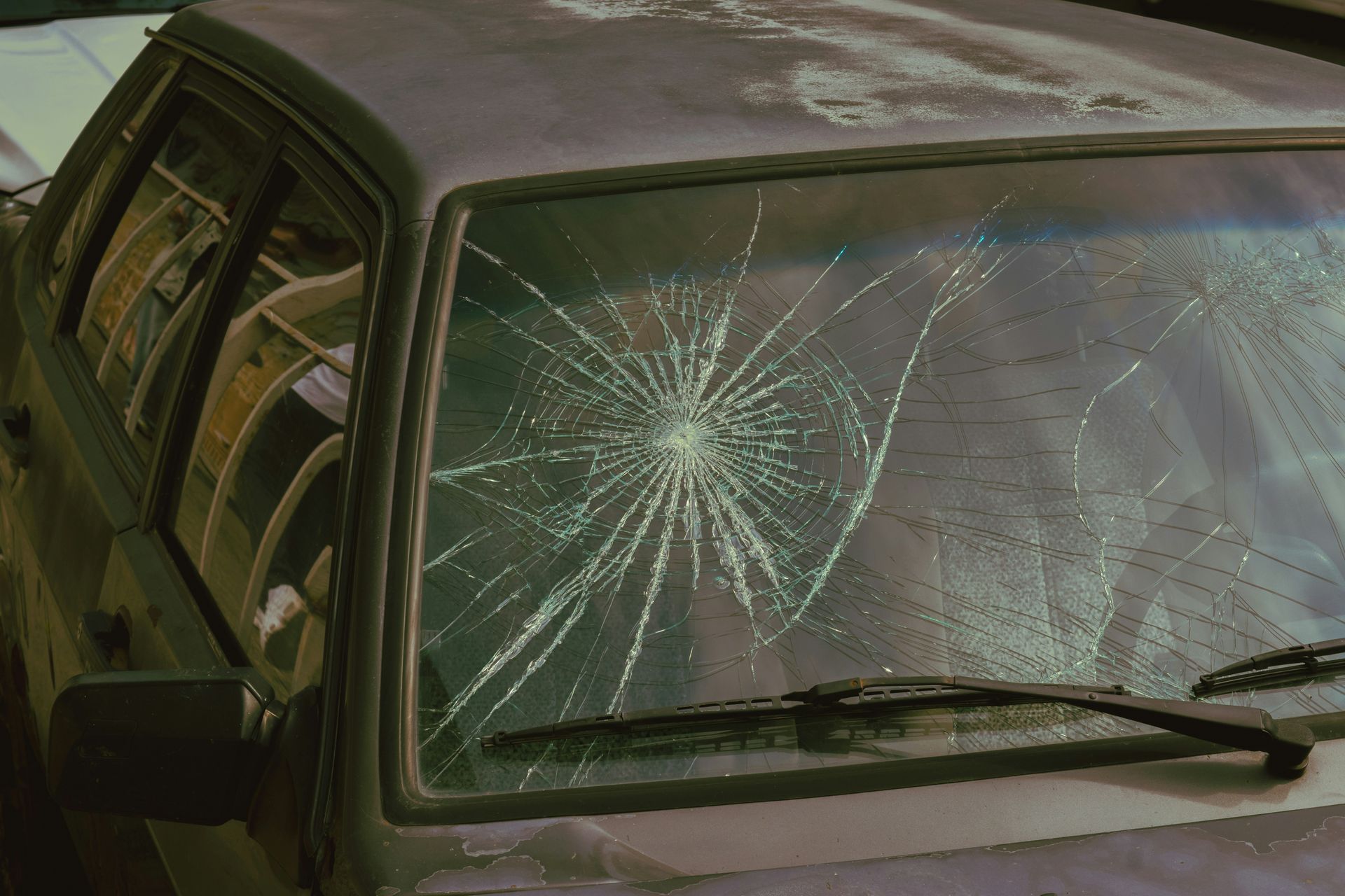 A car with a broken windshield is parked on the side of the road.