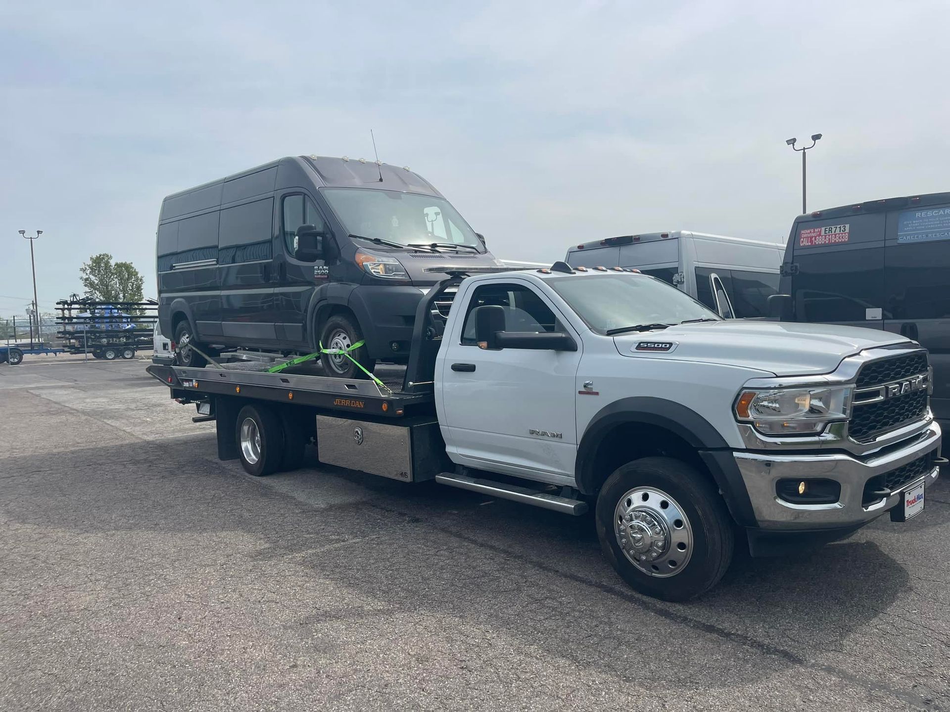 White tow truck carrying a dark van in a parking lot on a cloudy day.