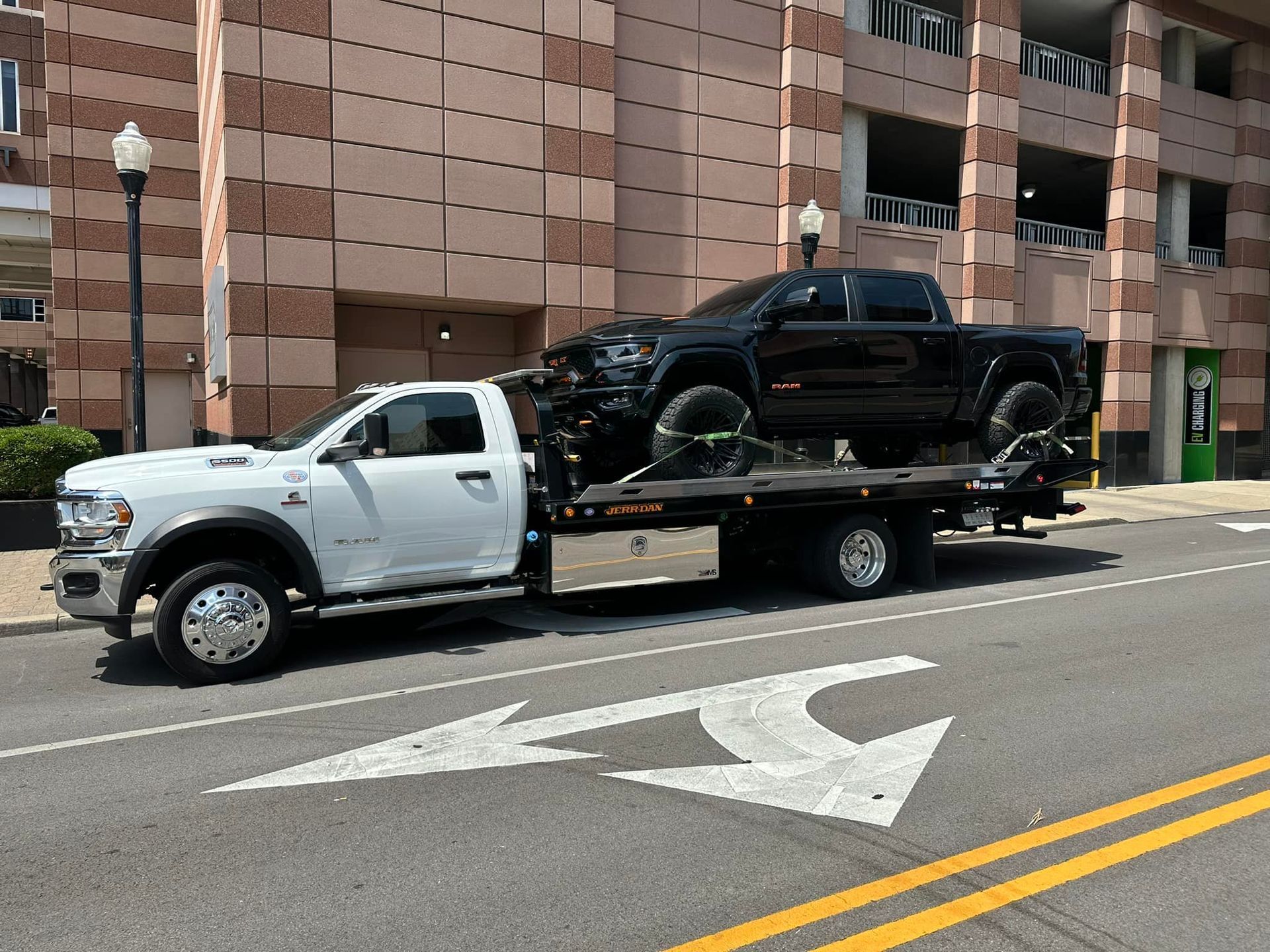 A black pickup truck loaded on a white tow truck on a city street.