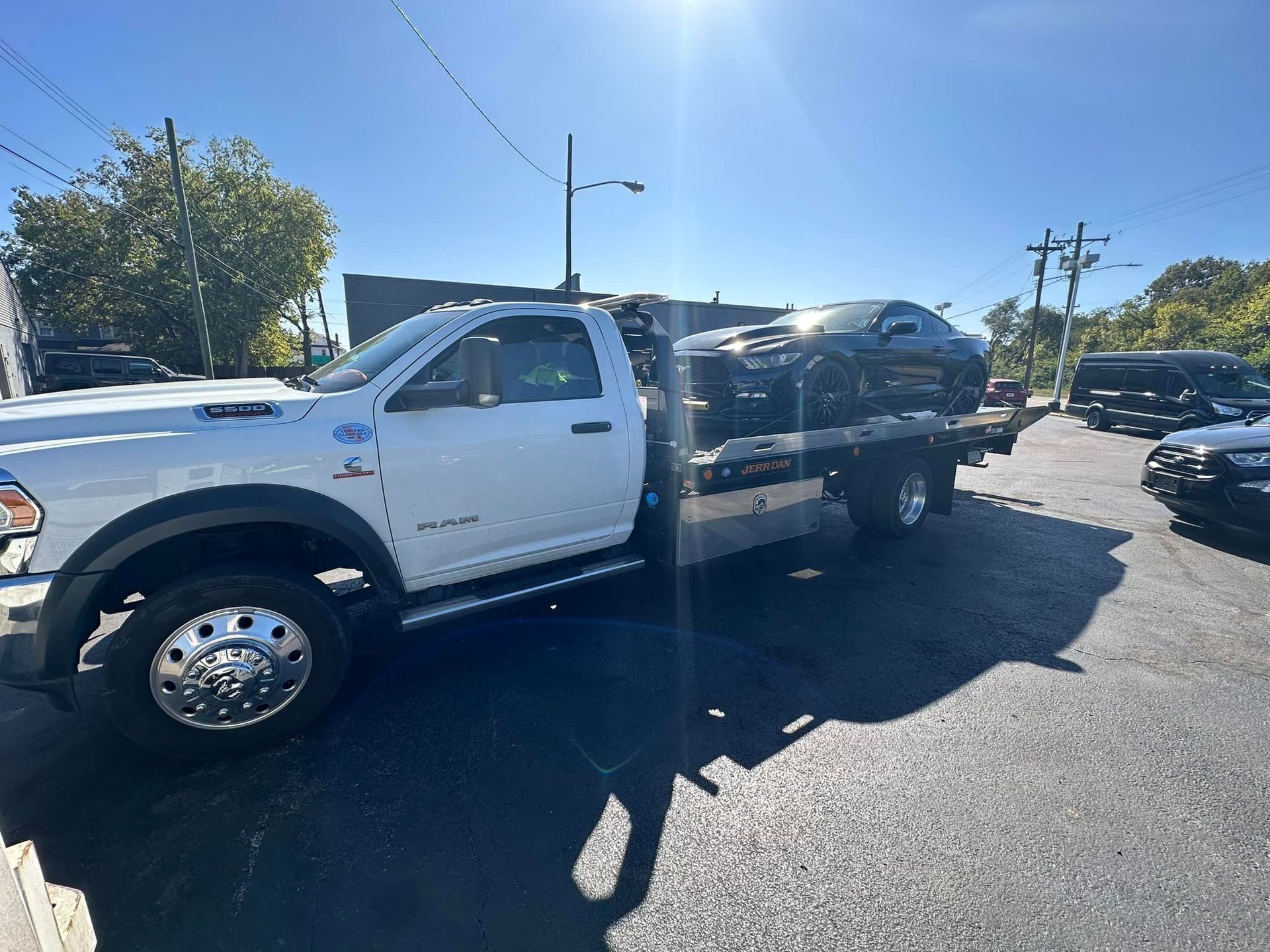White tow truck with a black car on its flatbed, parked on a paved road.
