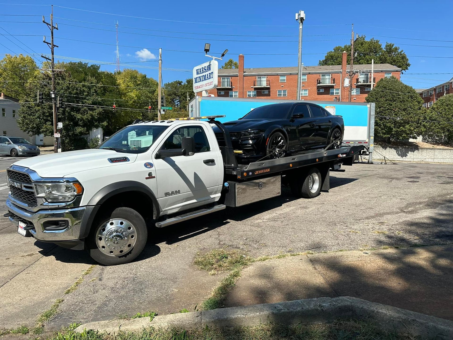 White tow truck hauling a black car, parked on gravel. Bright, sunny day.