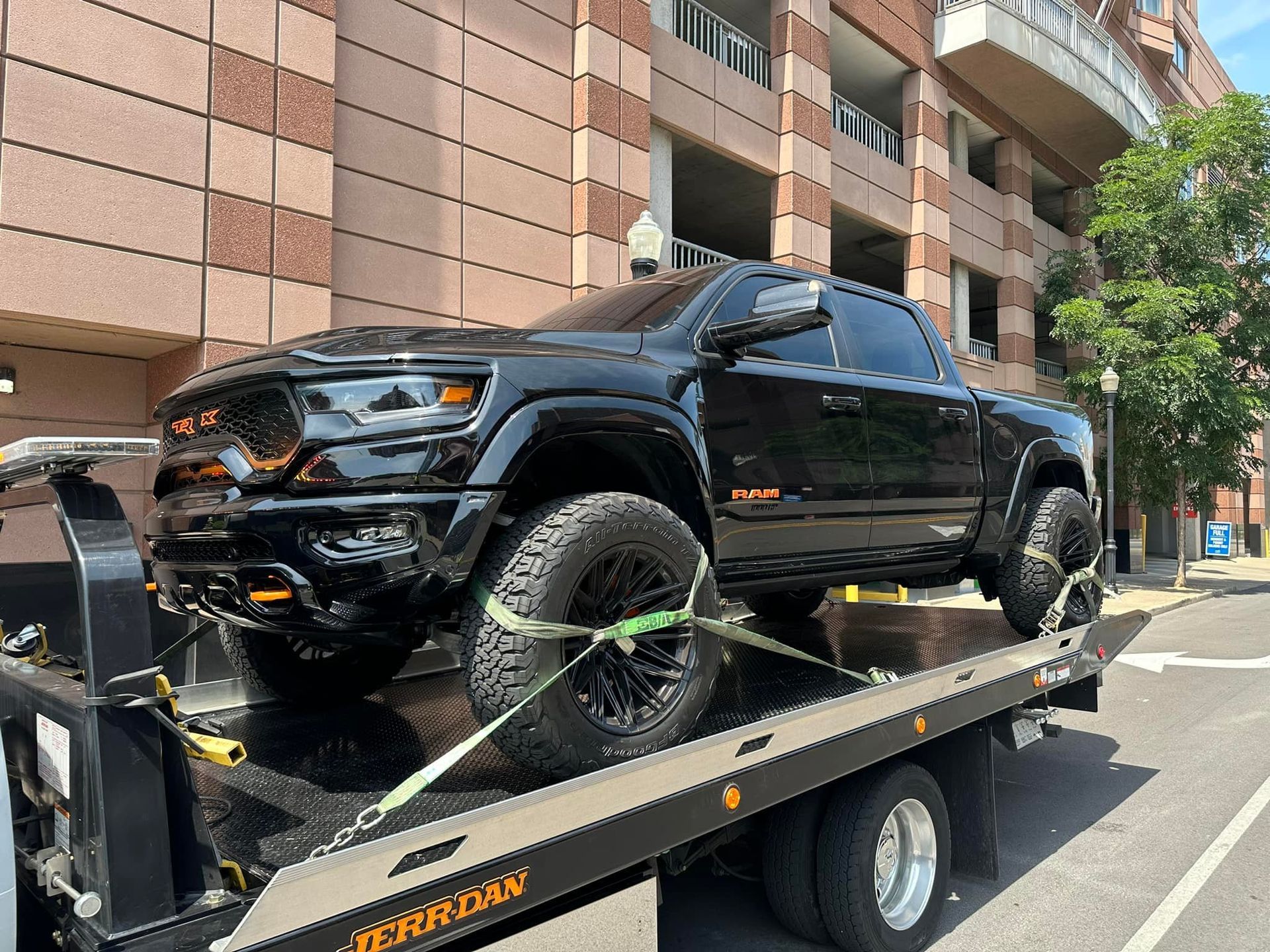 Black Ram TRX pickup truck on a flatbed tow truck on a city street.
