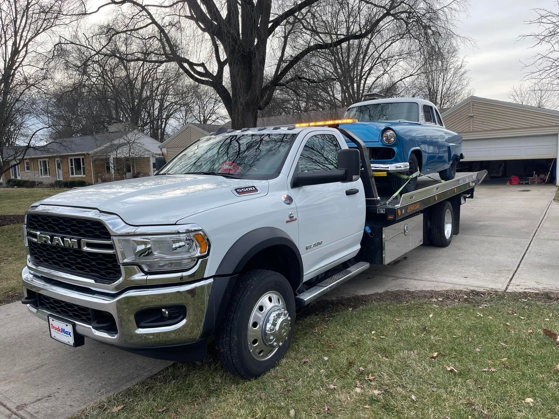 White tow truck transporting a blue vintage car on a residential street.