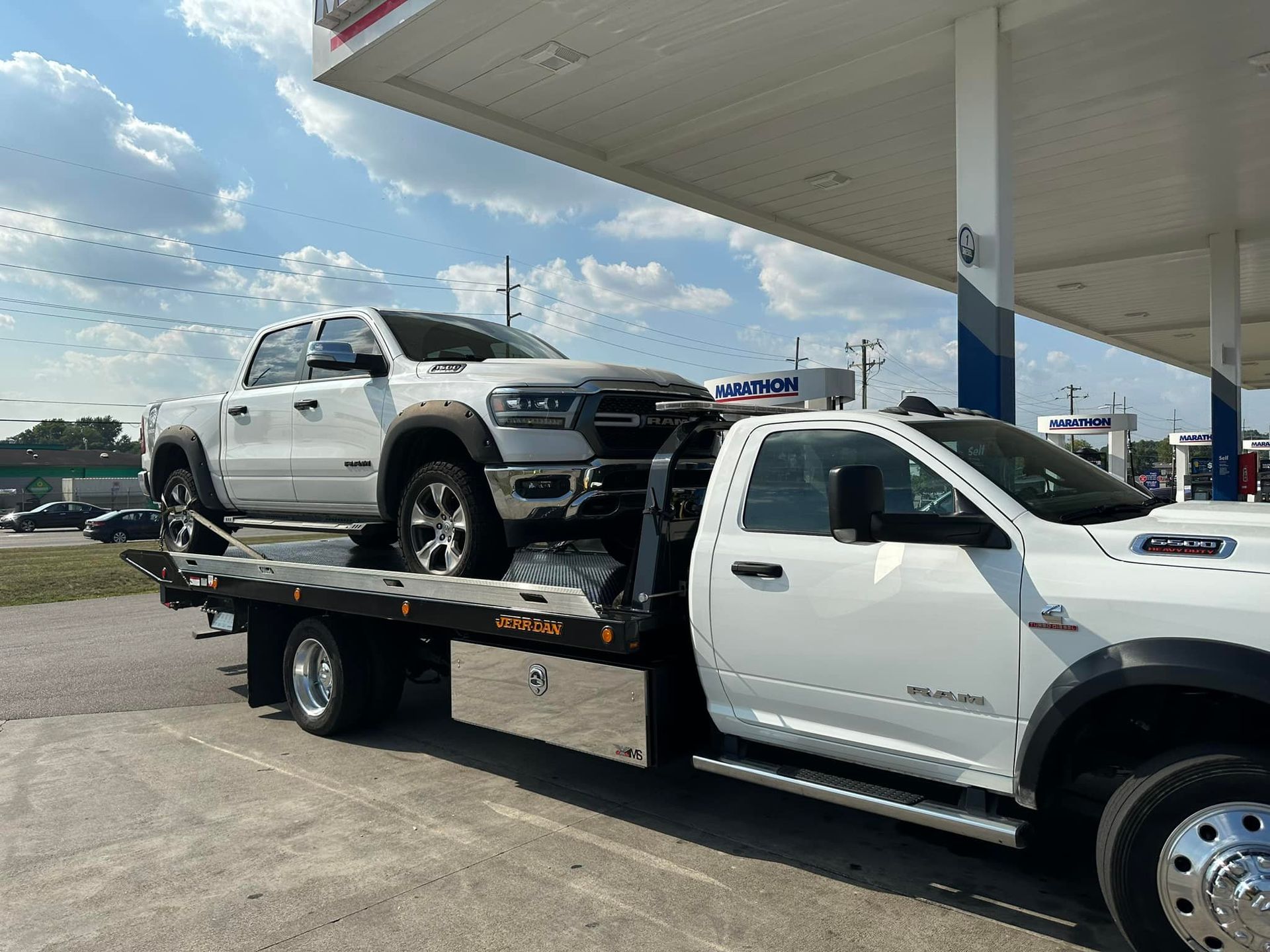 White pickup truck being towed by a flatbed tow truck at a gas station.