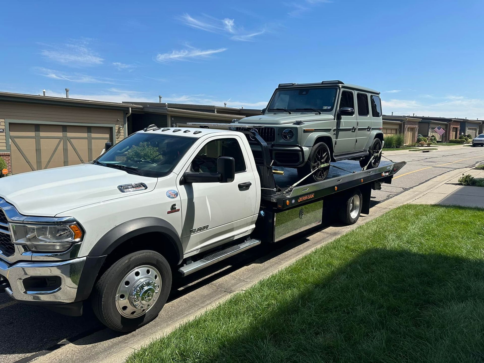 White tow truck hauling a gray Mercedes-Benz G-Class SUV on a sunny residential street.