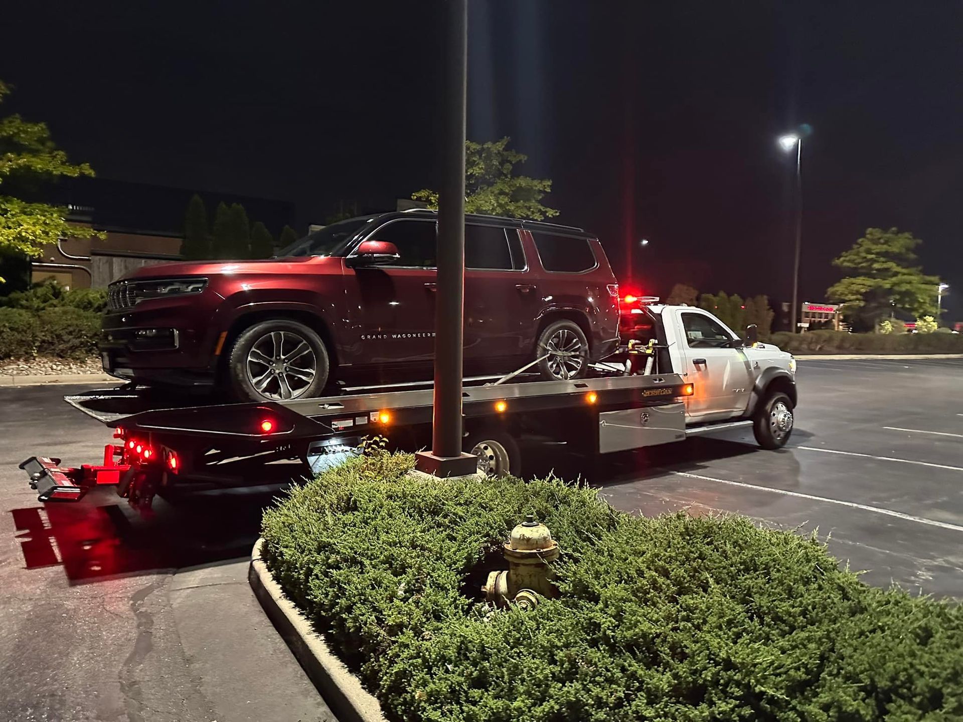 Red SUV on a tow truck in a parking lot at night, tow truck lights on.