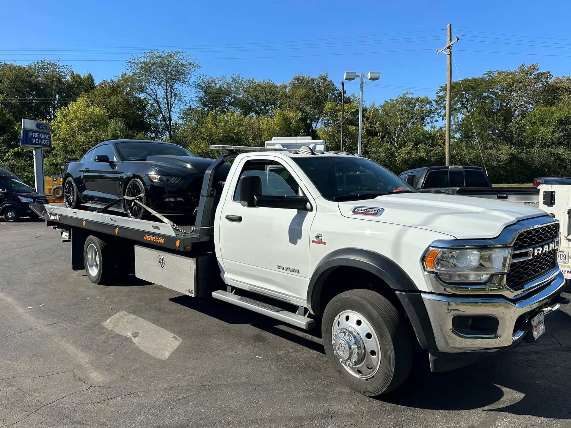 White tow truck hauling a black sports car on a sunny day.