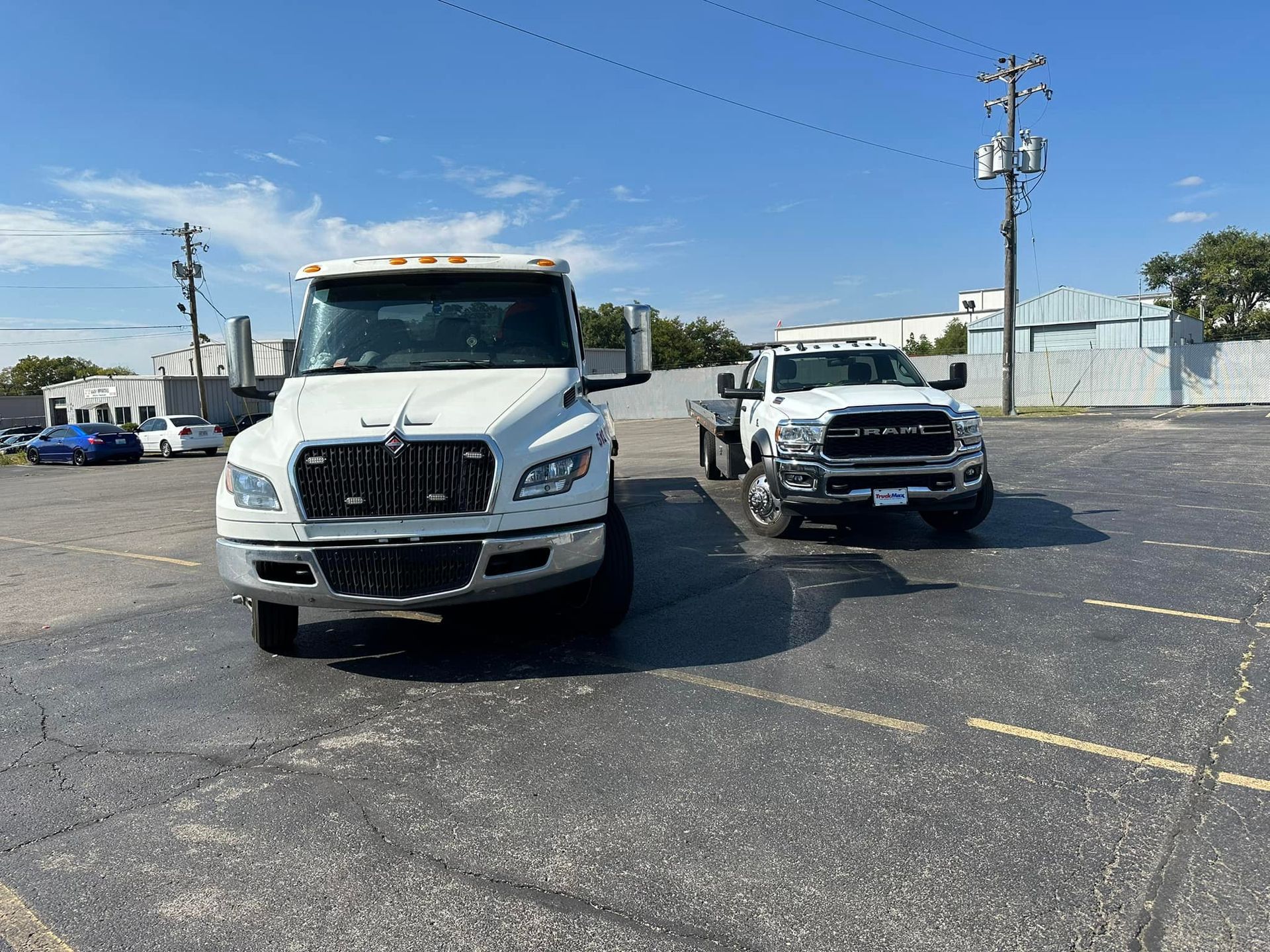 White tow truck and a smaller white pickup truck parked in a parking lot on a sunny day.