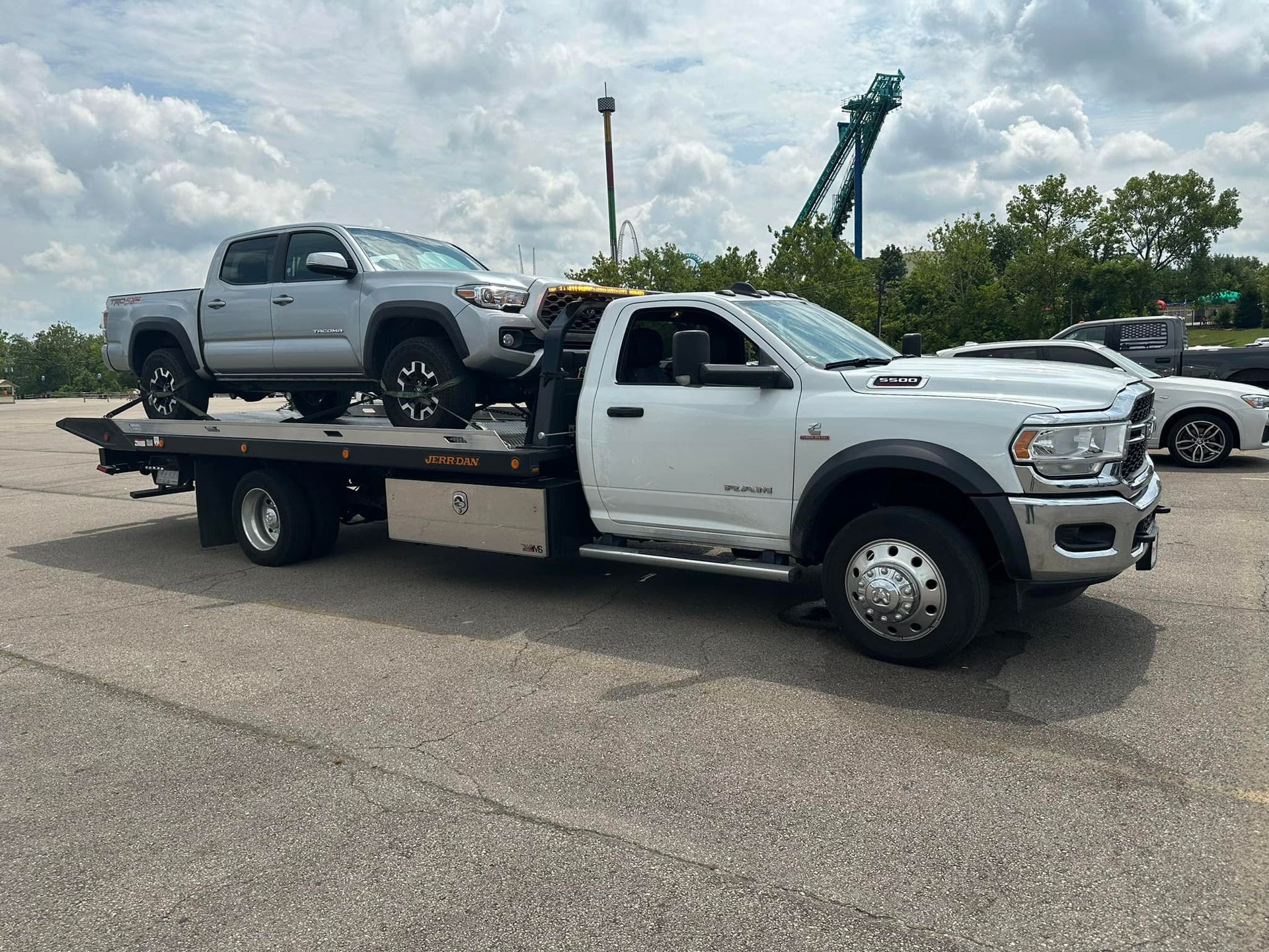 A white tow truck carrying a silver pickup truck on a sunny day.