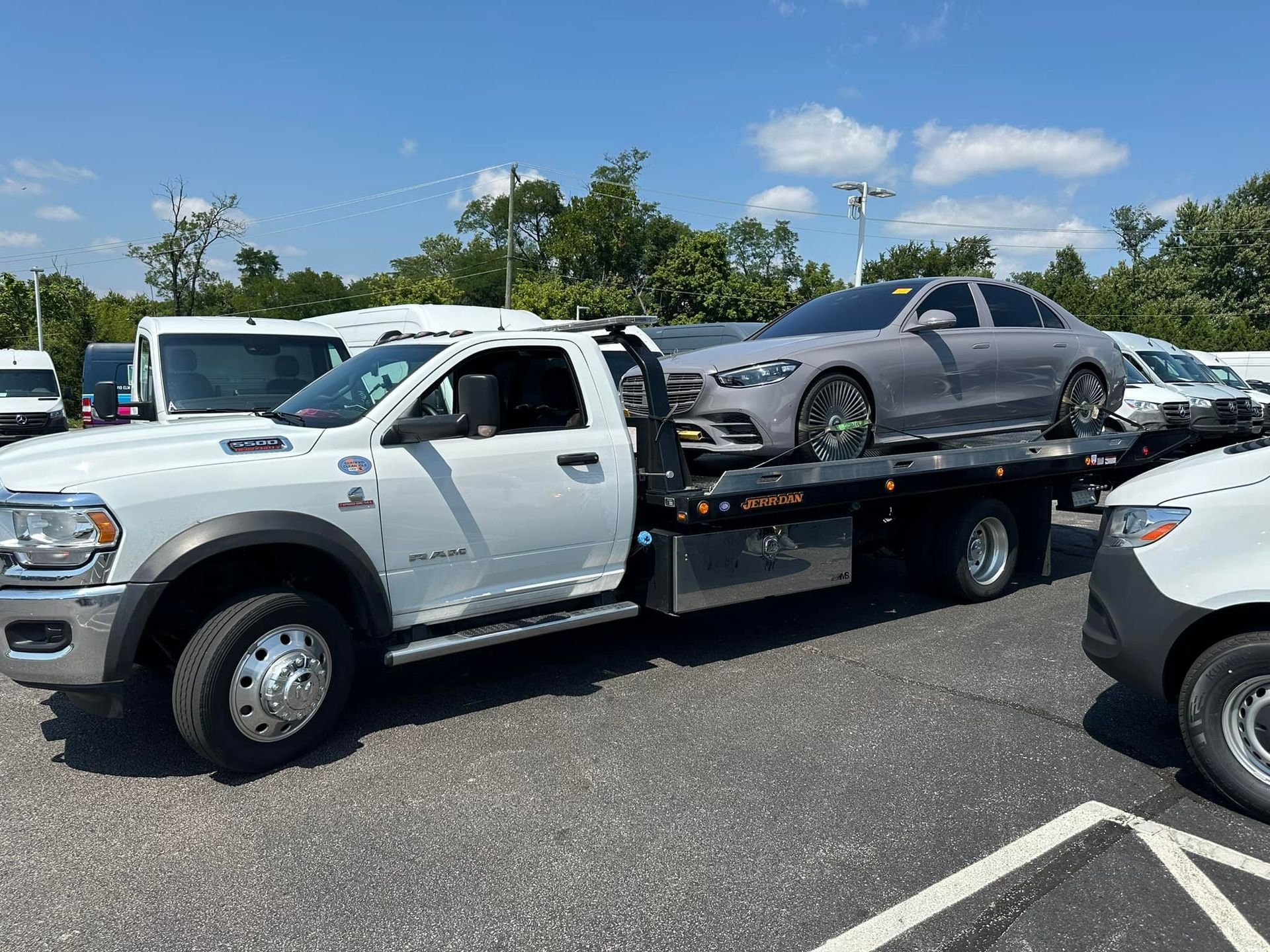 A gray car loaded on a white tow truck in a parking lot on a sunny day.