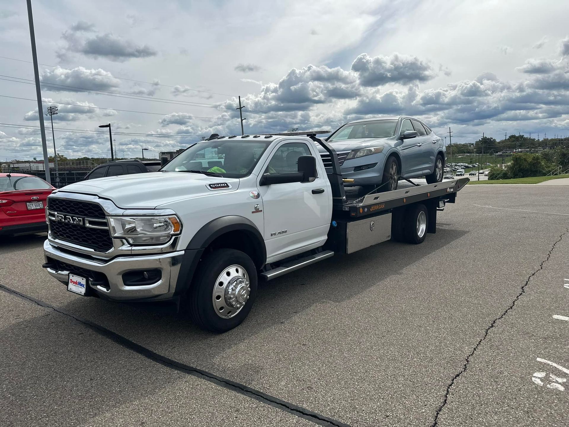 White tow truck with a gray car on its flatbed in a parking lot.