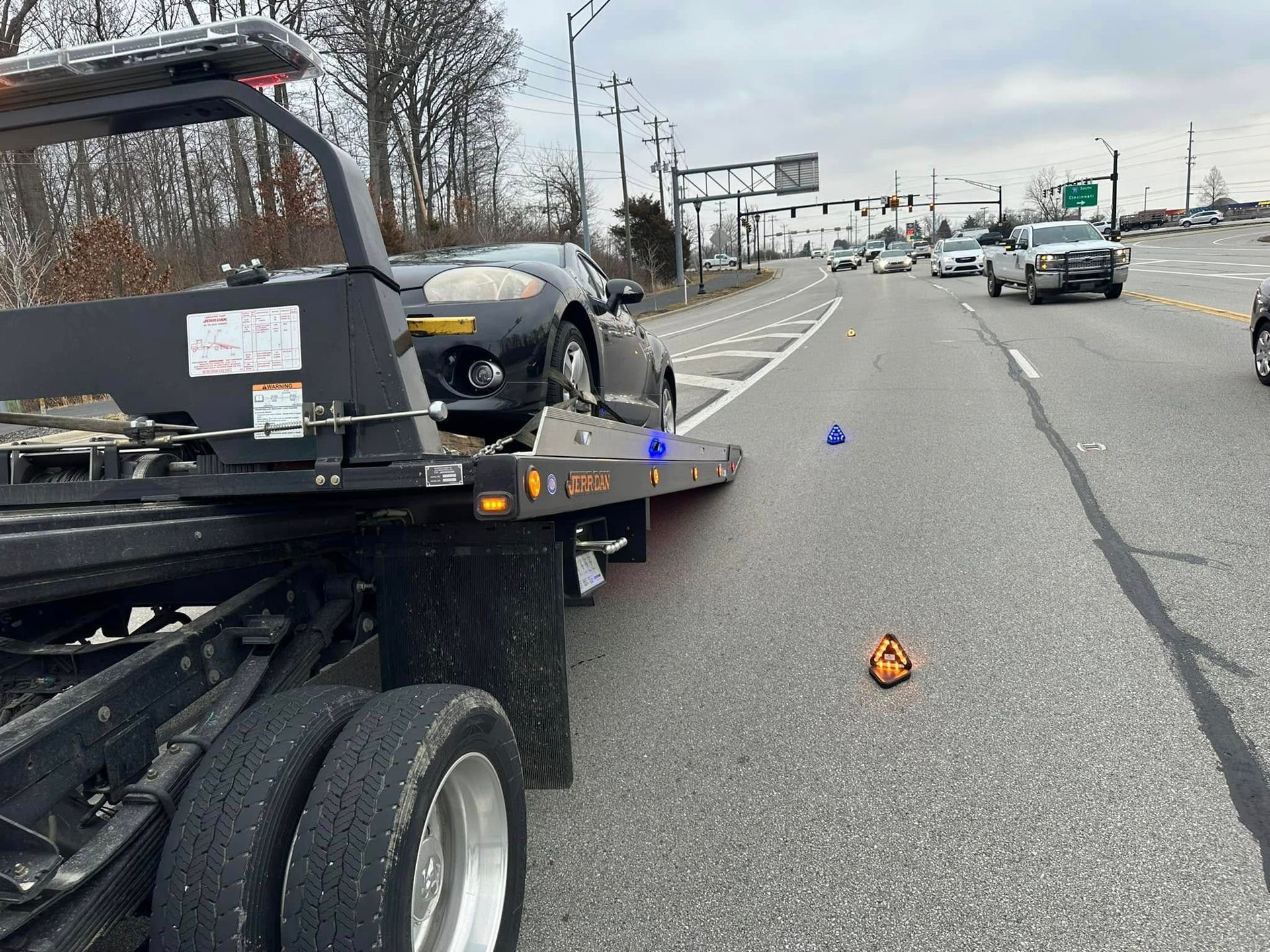 A black car on a tow truck on a multilane highway with police activity.