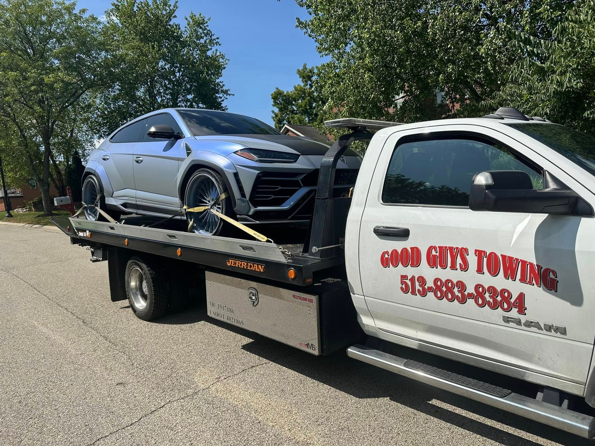 A gray Lamborghini SUV being towed on a flatbed truck labeled 