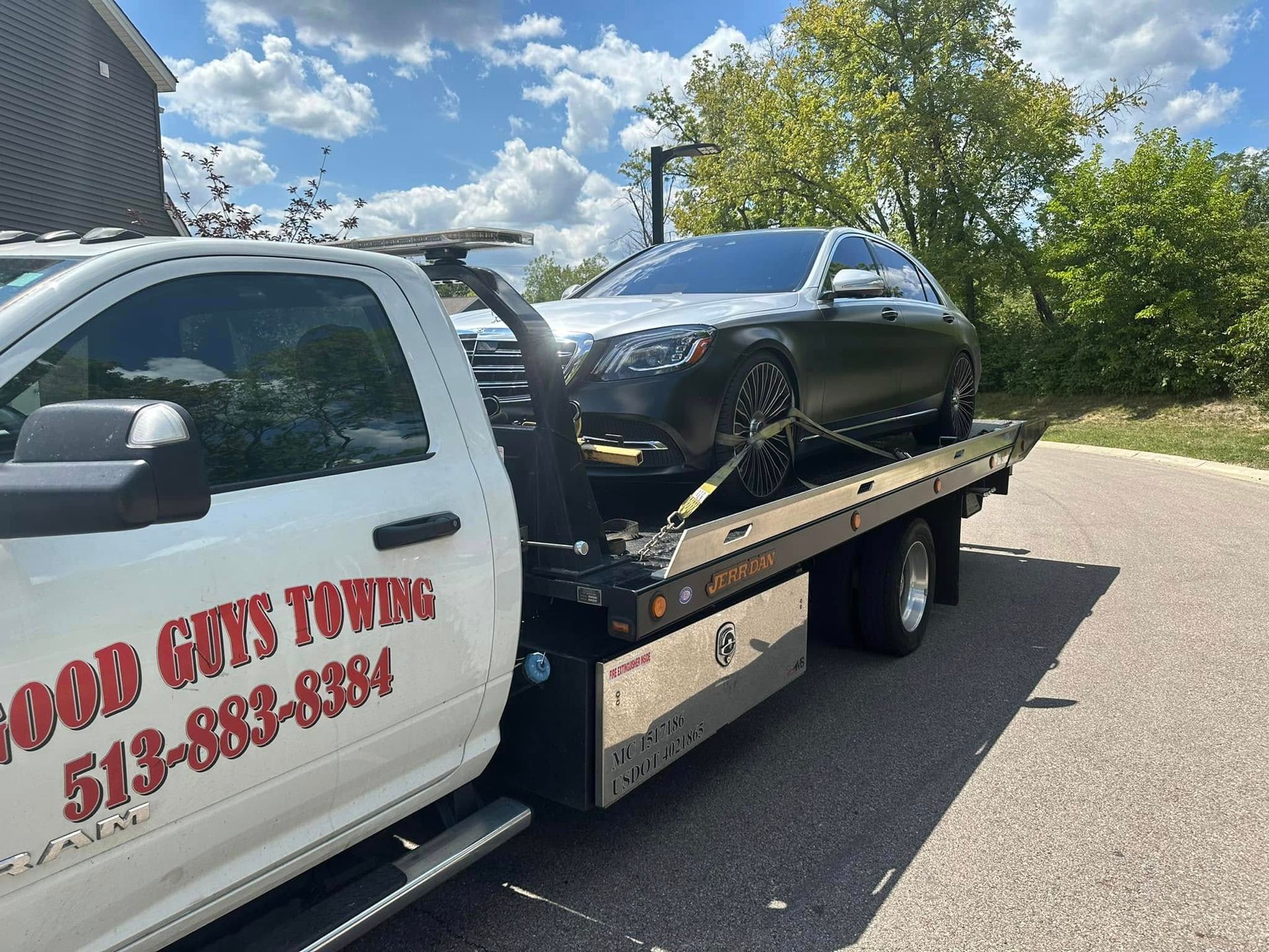 Tow truck with a silver car on its flatbed, parked outdoors. The truck is white with red text.