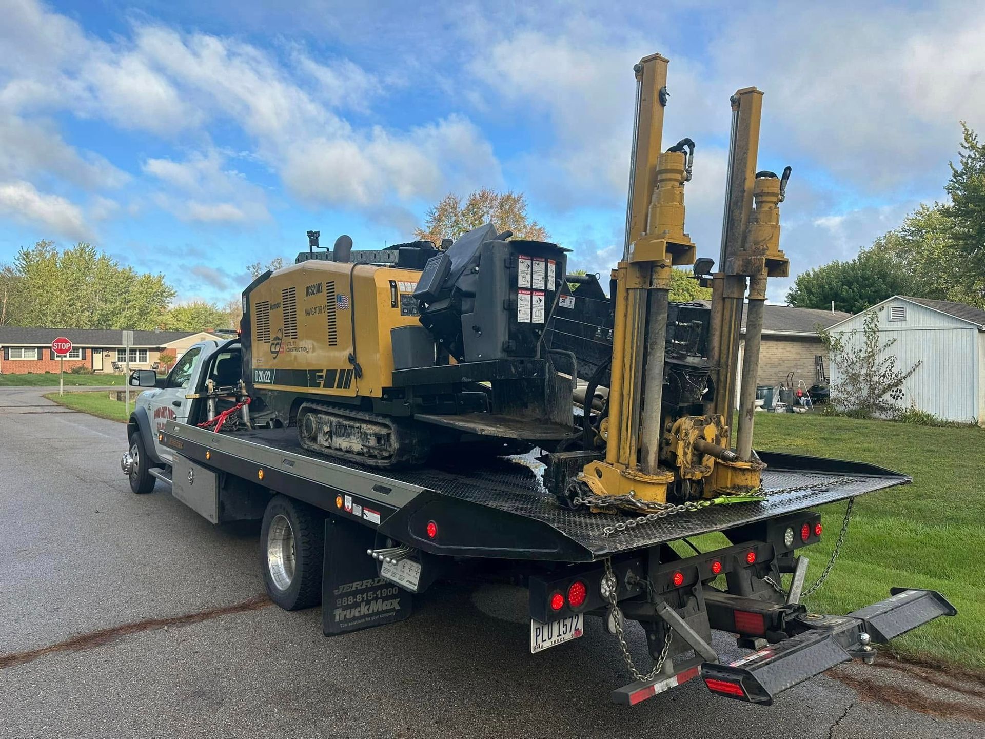 Yellow drilling machine on a flatbed truck, parked on a street near houses.