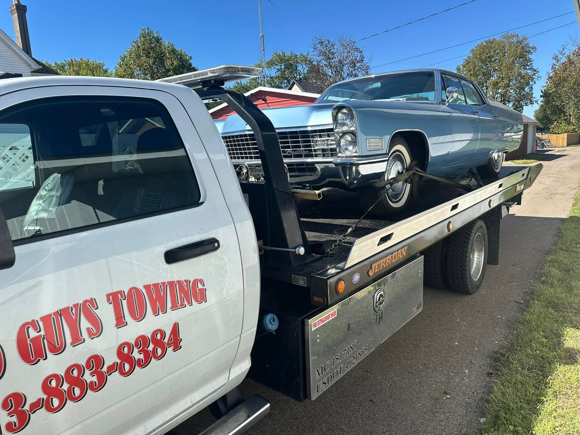 A light blue classic car being towed on a flatbed truck by 