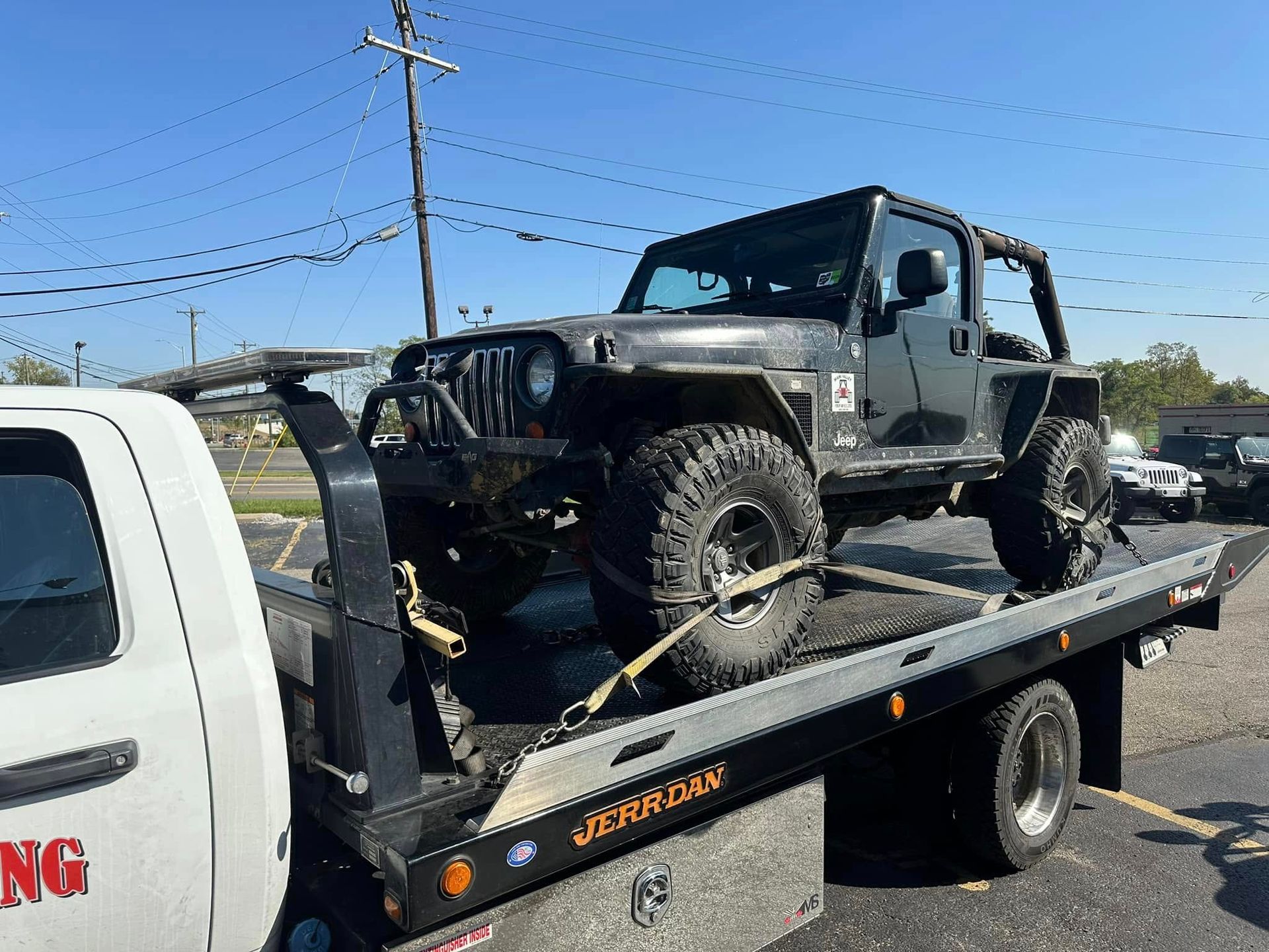 A black Jeep being towed on a flatbed tow truck on a sunny day.