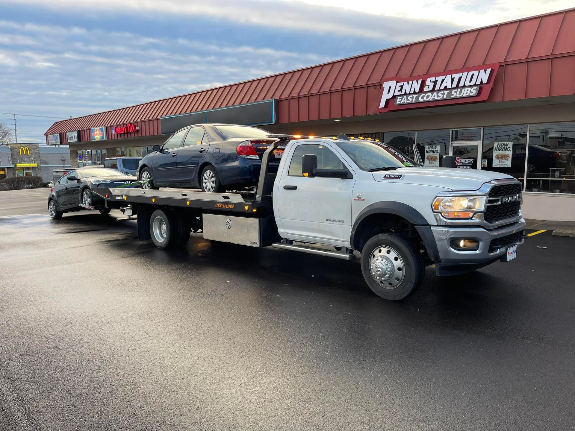 Tow truck with two cars on it, in front of Penn Station restaurant.
