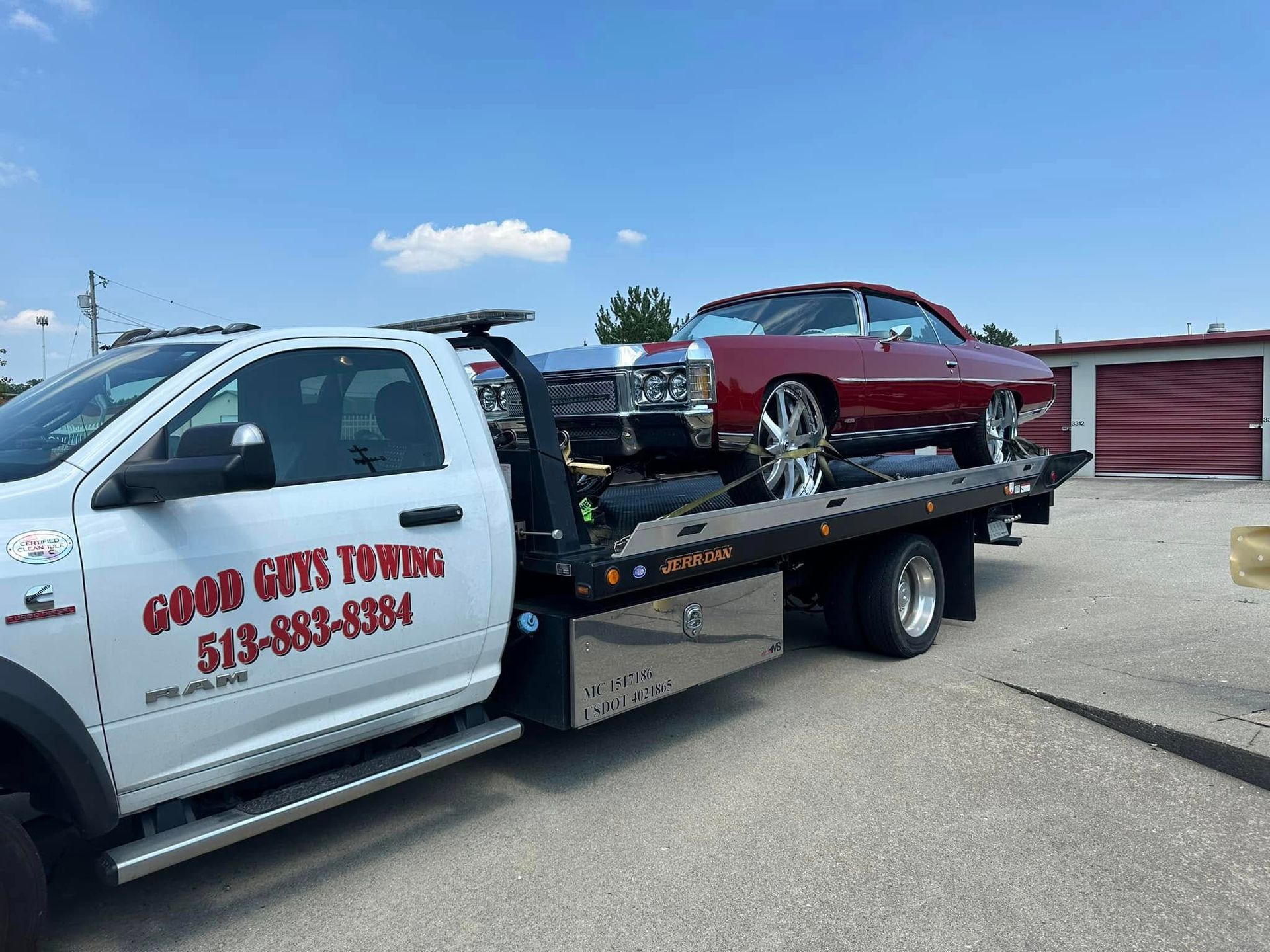 Tow truck carrying a maroon classic car on a sunny day. 