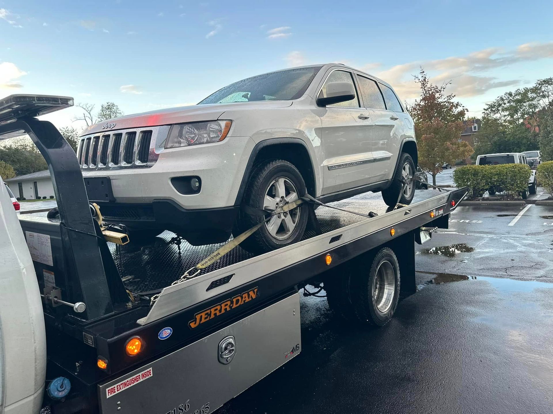 White Jeep SUV on a tow truck in a parking lot, likely being towed.