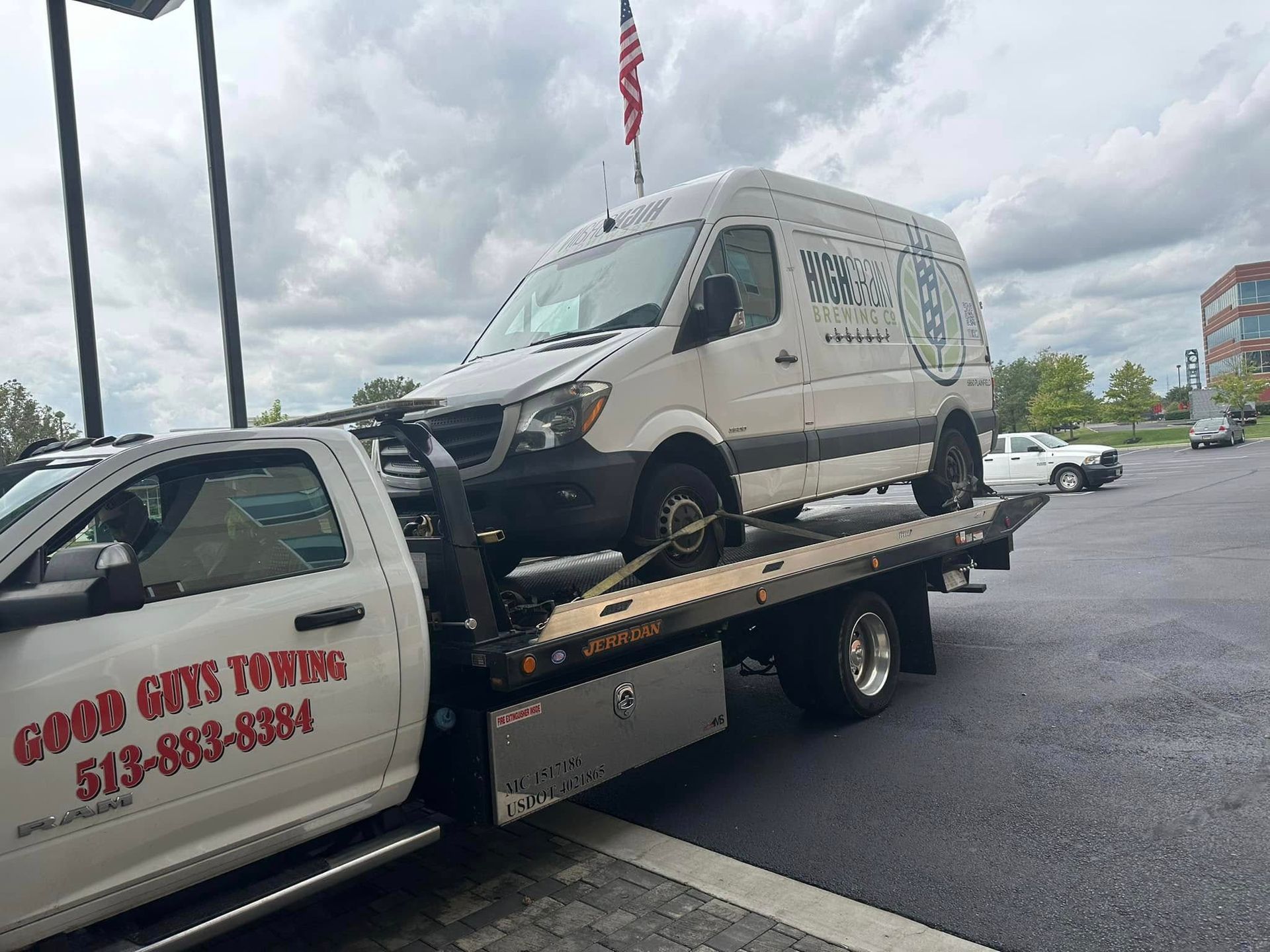A white van being towed by a tow truck, with the Good Guys Towing logo visible on the truck.