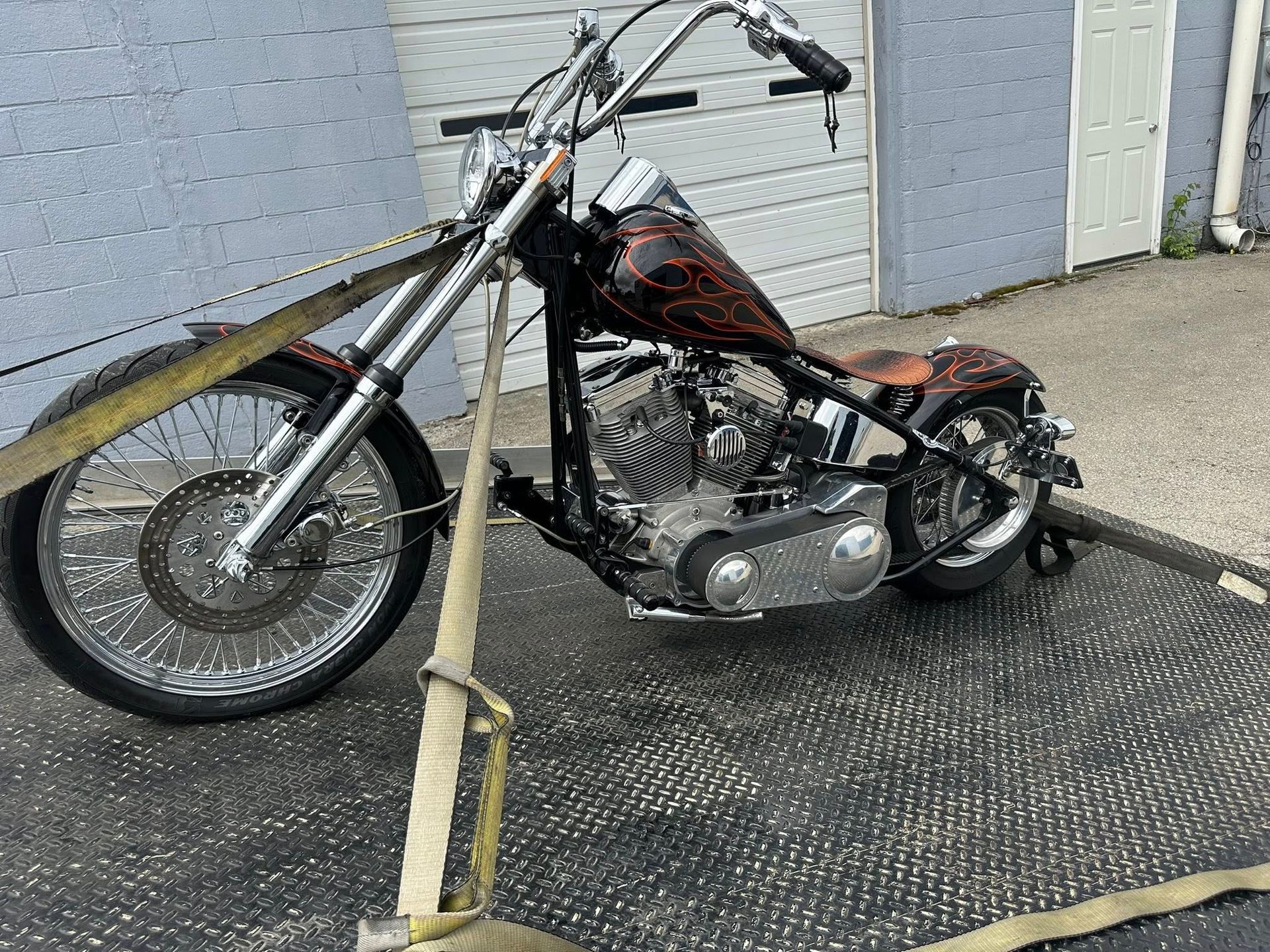 Chopper motorcycle secured on a tow truck bed, displaying custom flame paint and chrome detailing.