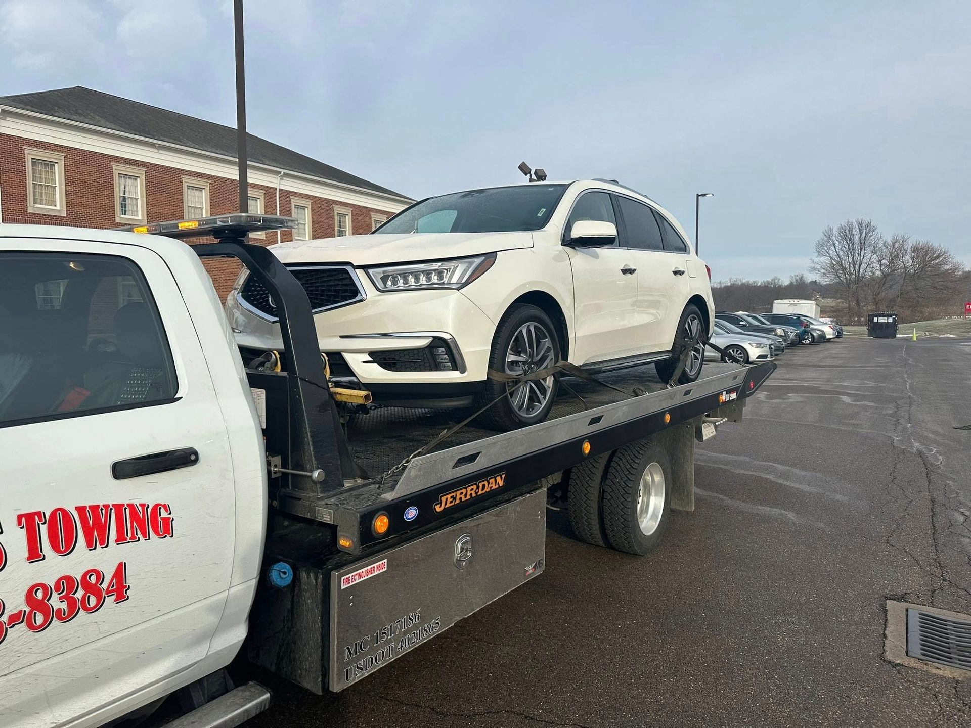 White SUV being towed on a flatbed tow truck. Buildings and other cars in the background.