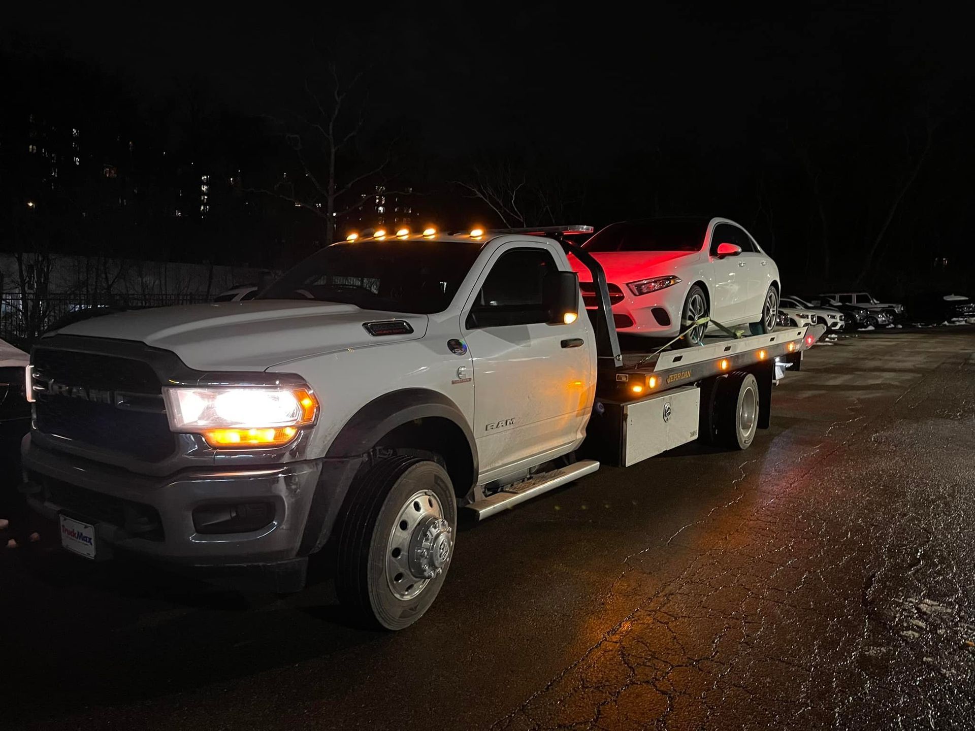 White tow truck at night, carrying a white sports car with red taillights.