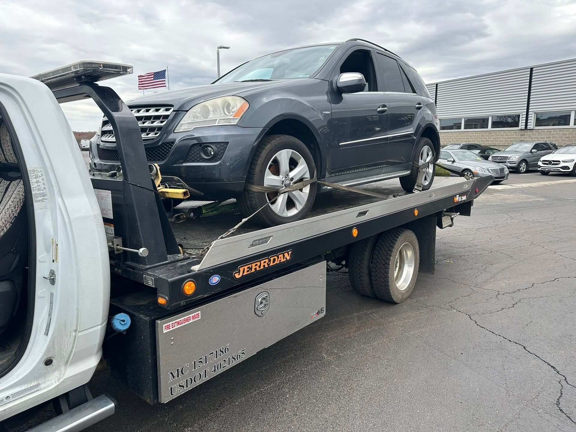 Mercedes SUV being towed on a flatbed tow truck on an overcast day.