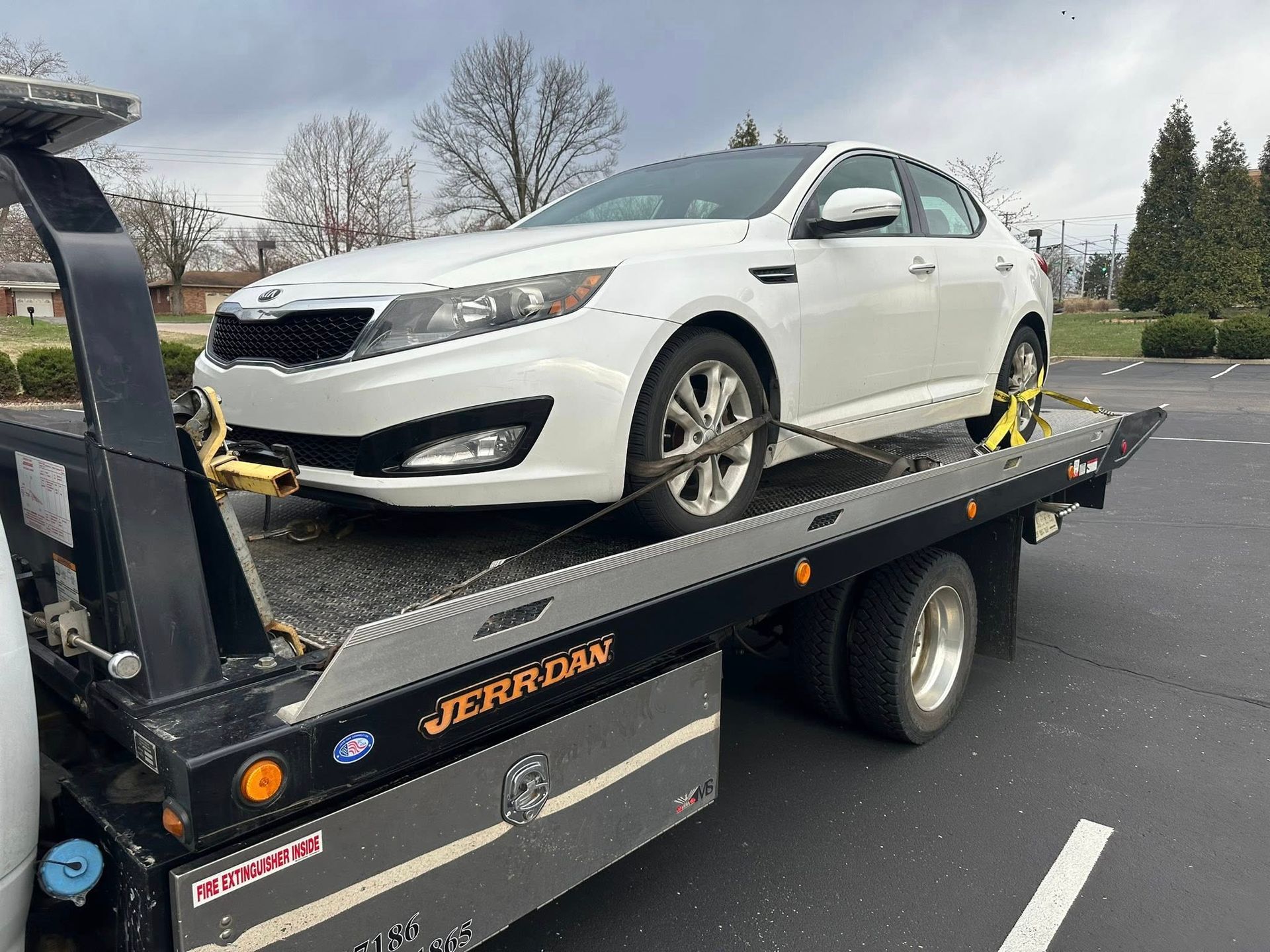 White car being towed on a flatbed tow truck in a parking lot.