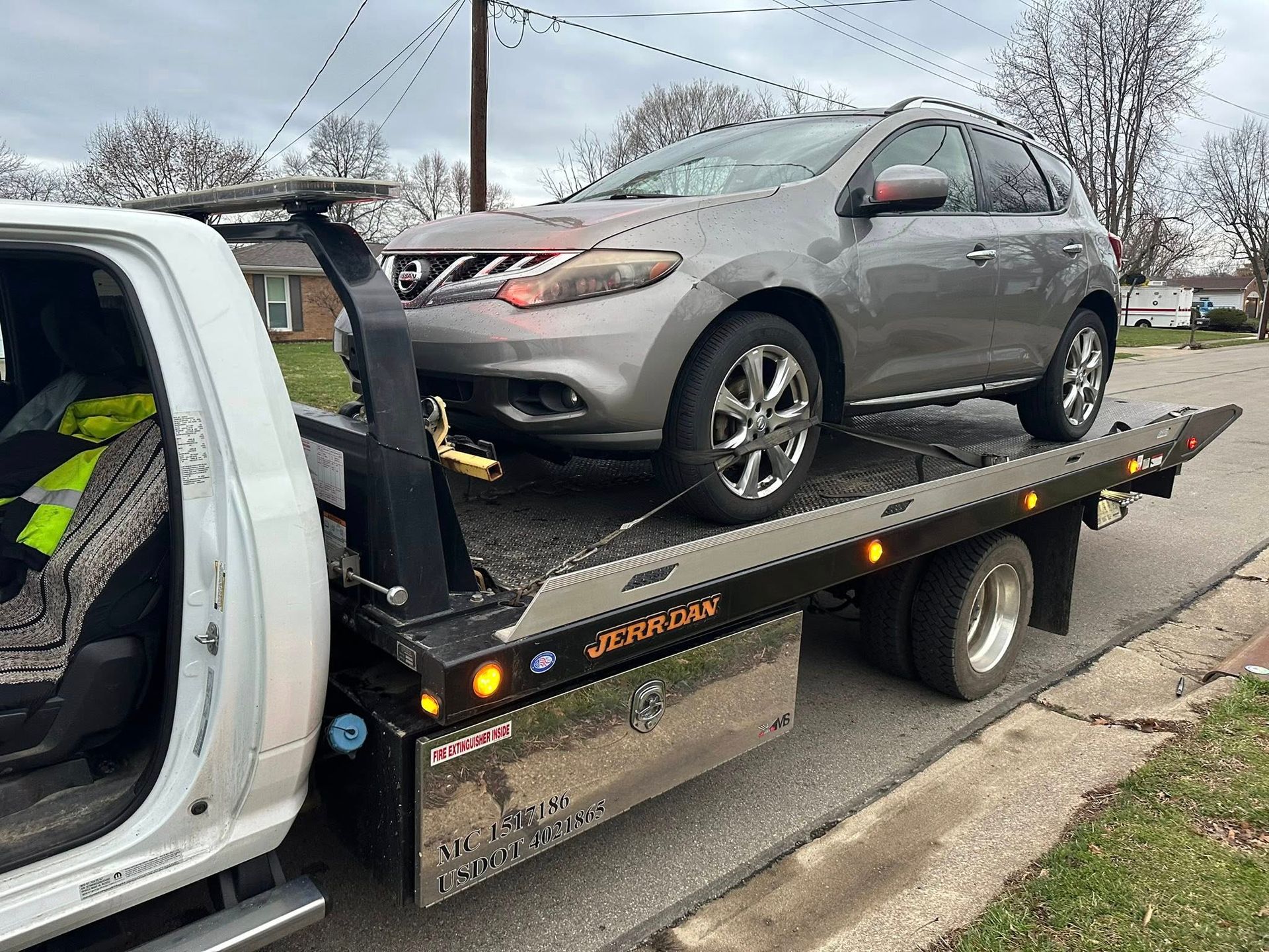 Gray SUV being towed on a flatbed tow truck. Daytime scene on a residential street.