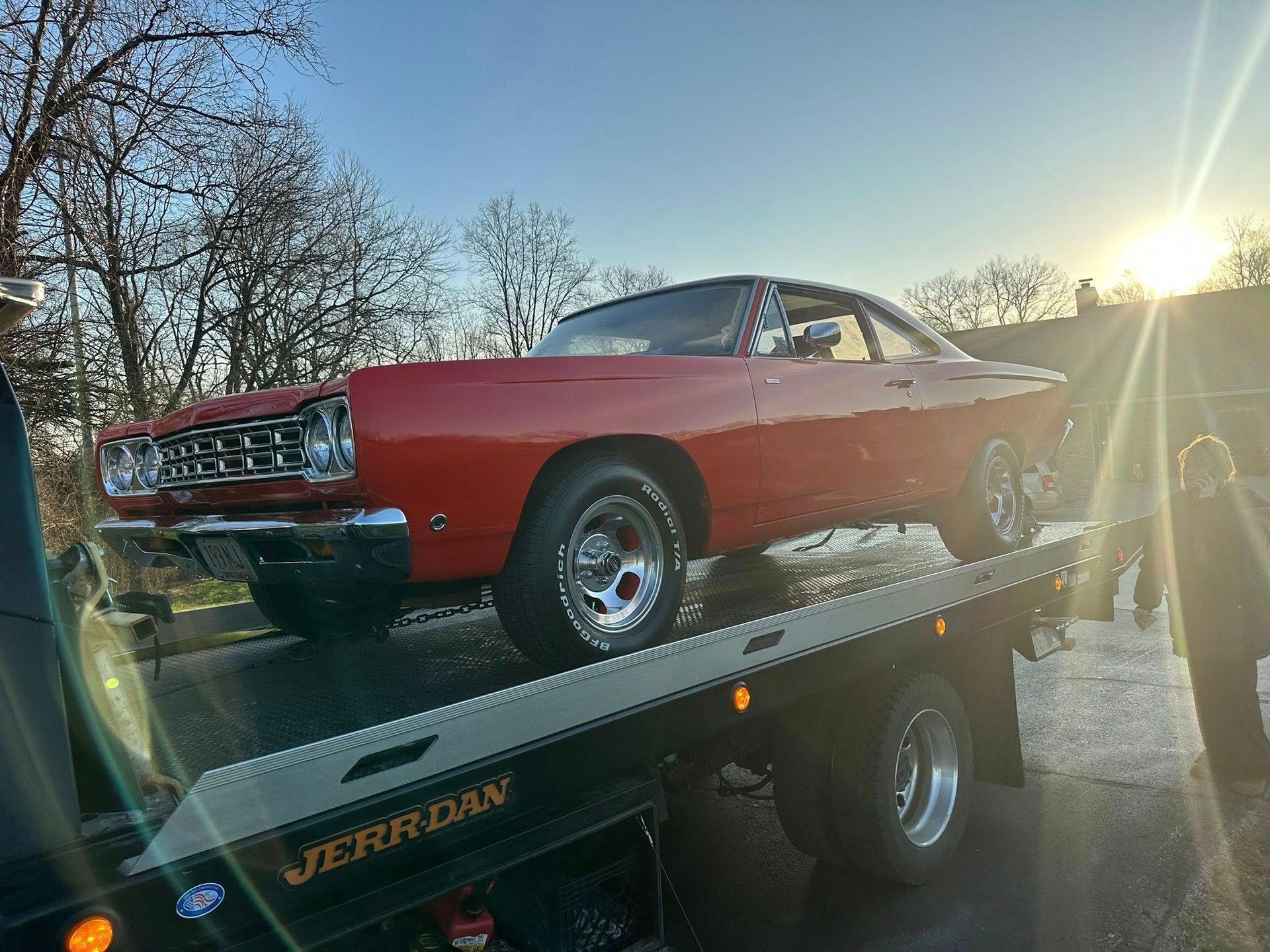Red classic car on a tow truck at sunset.