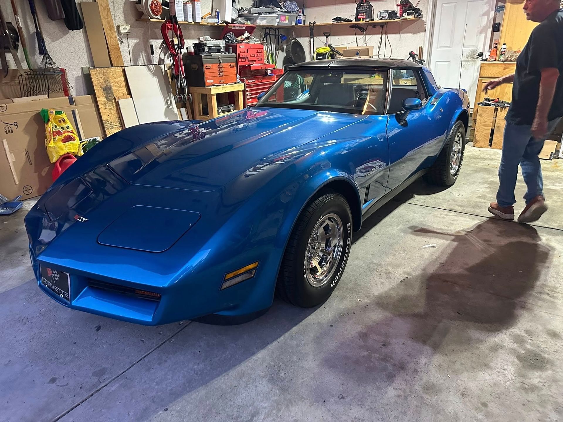 Blue classic Corvette in a garage, person stands nearby.