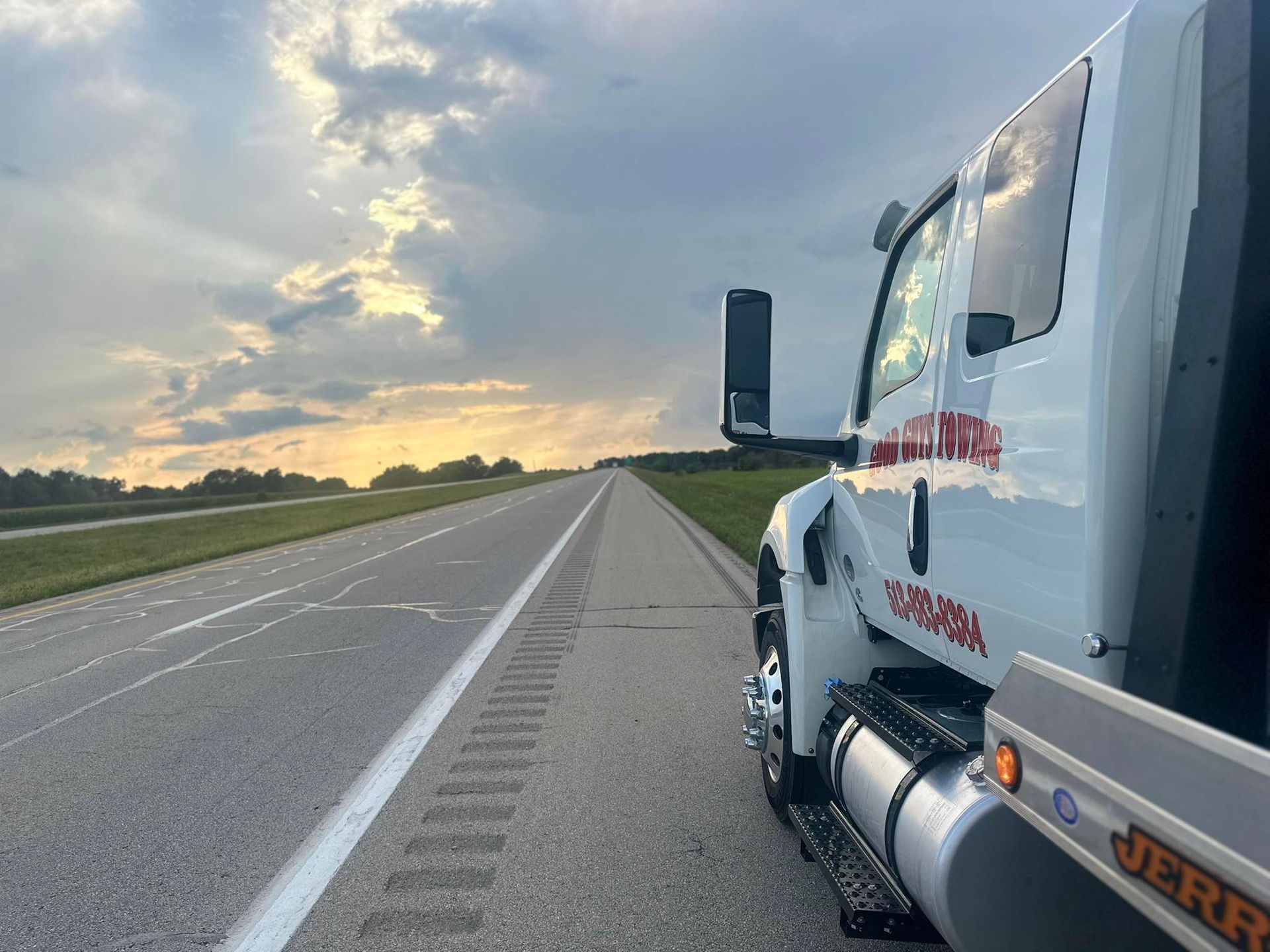 Tow truck parked on the shoulder of a highway at sunset.