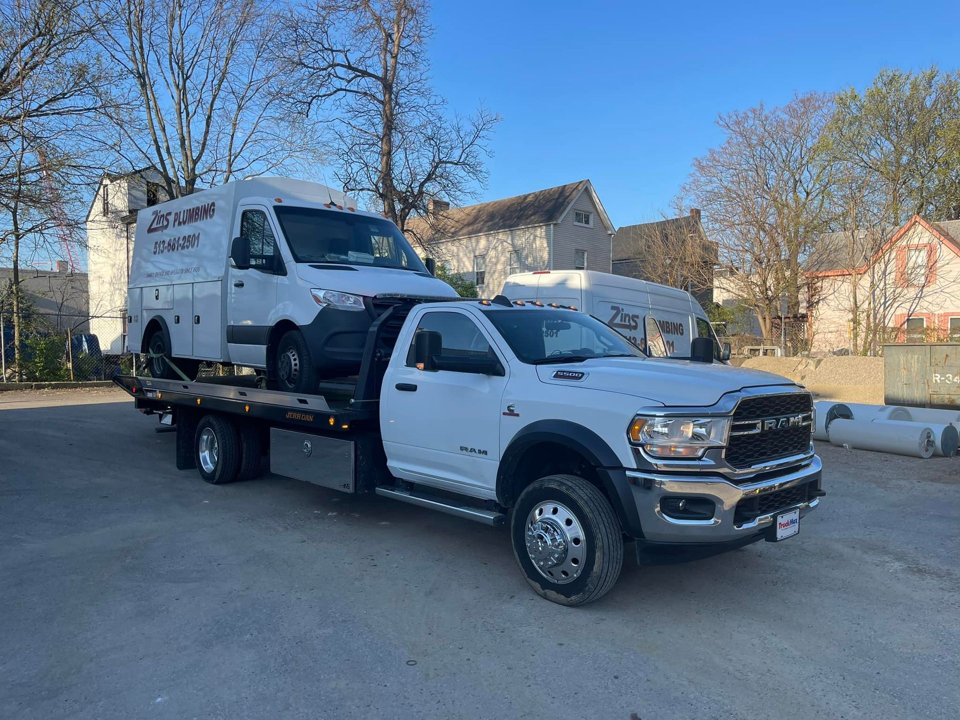 White tow truck carrying a white van. Outdoors, daytime, next to a building.