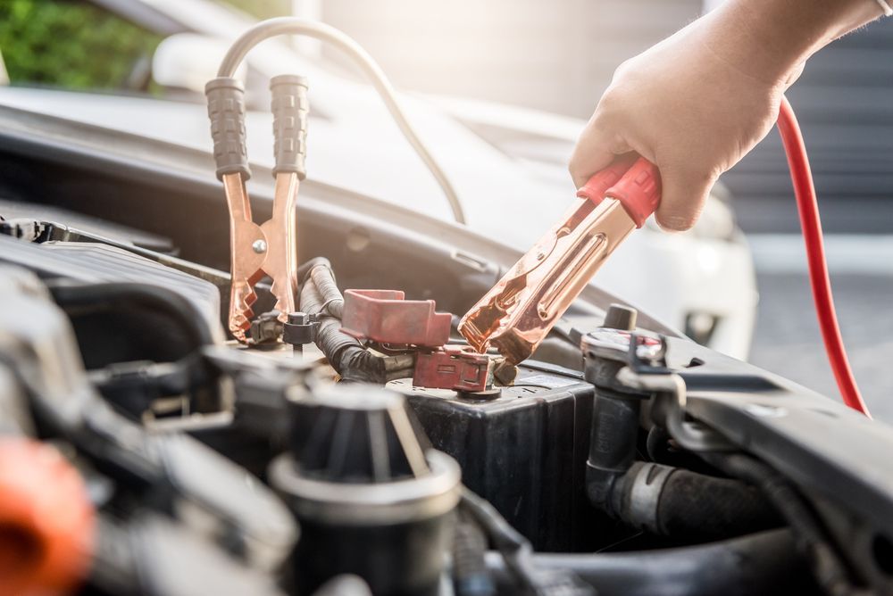 Hand connecting red jumper cable to a car battery terminal.