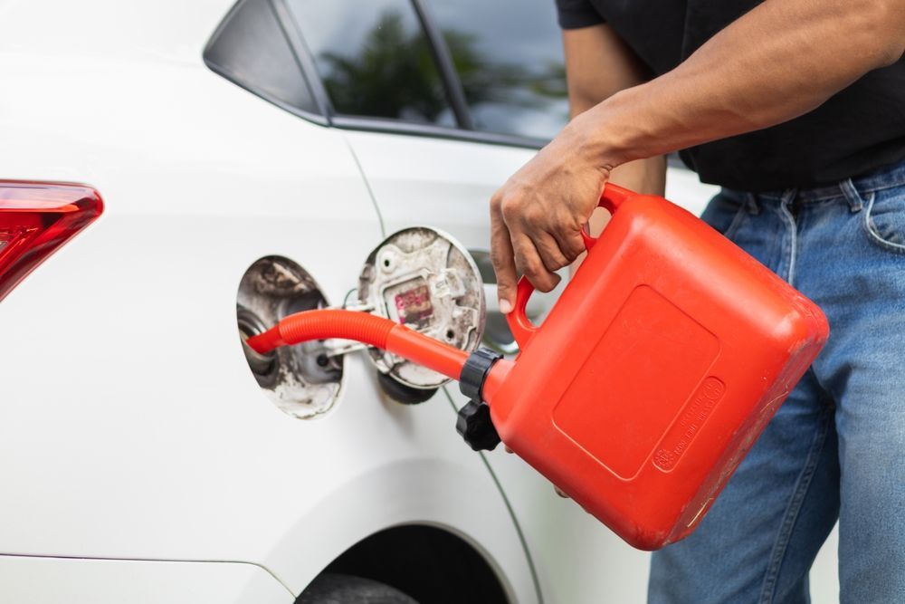 Person filling a white car's gas tank with a red gas can.