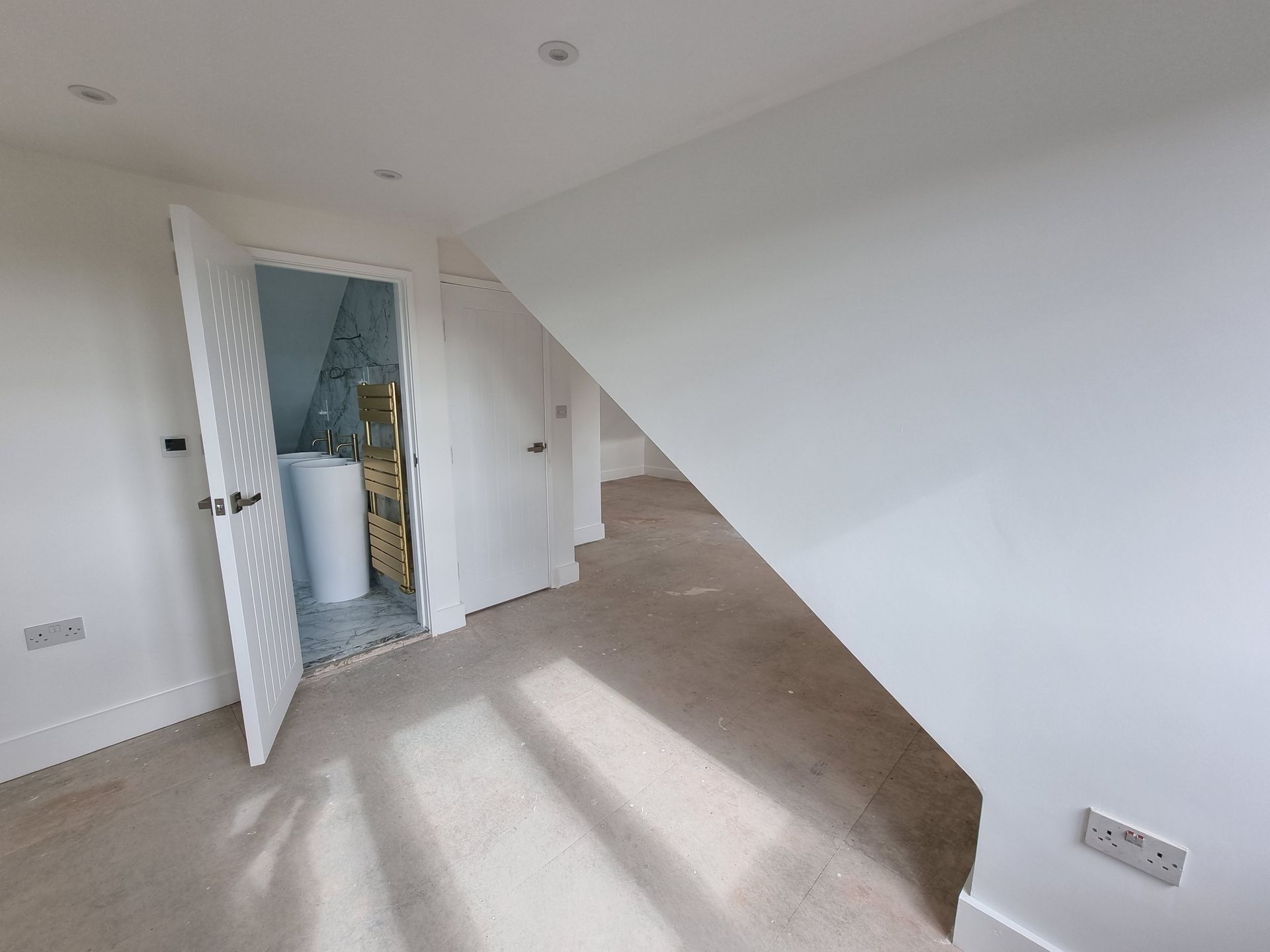 An empty room with a slanted ceiling and a bathroom in the corner.