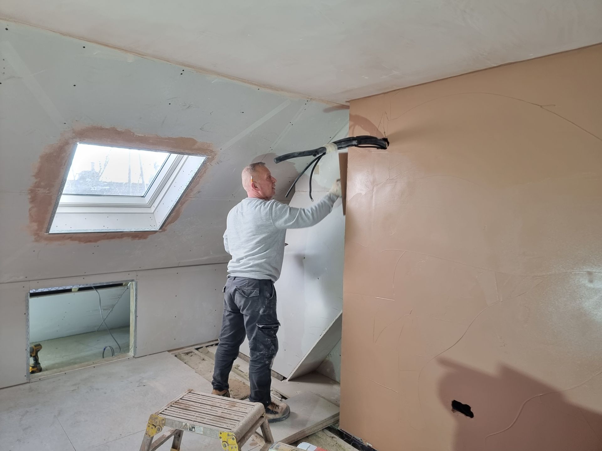 A man is working on a wall in a room with a skylight.