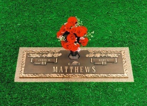Bronze grave marker with red flowers on green grass, engraved with the name Matthews