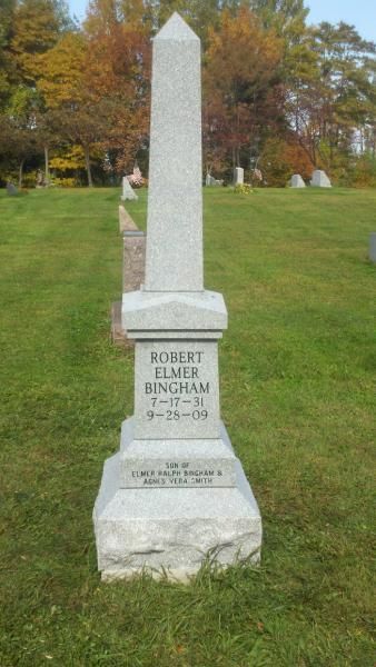 Tall white gravestone in a grassy cemetery with autumn trees in the background