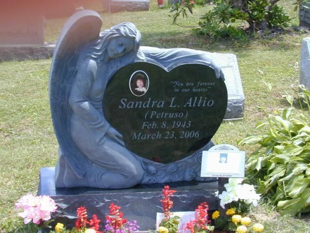 Blue angel statue beside a black memorial headstone with flowers in a cemetery