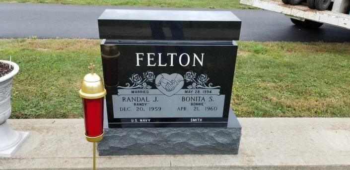 Black granite gravestone marked “FELTON” with a red-and-gold cemetery vase beside it.