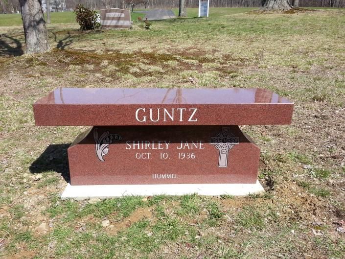 Brown memorial bench gravestone engraved “GUNTZ” in a grassy cemetery.