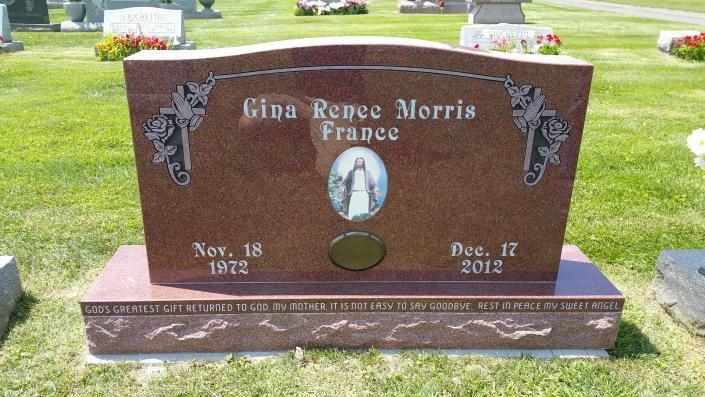 Pink granite gravestone in a cemetery with engraved portrait and dates, surrounded by green grass.