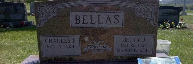 Gravestone with “BELLAS” engraved, flanked by plaques for Charles F. and Betty J. in a cemetery.