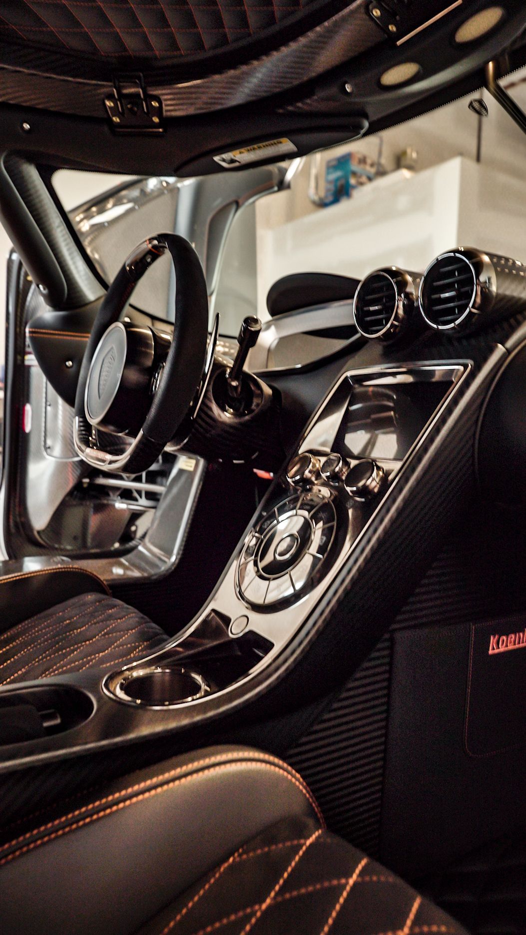 Luxurious car interior with black and orange leather, carbon fiber accents, and polished silver details.
