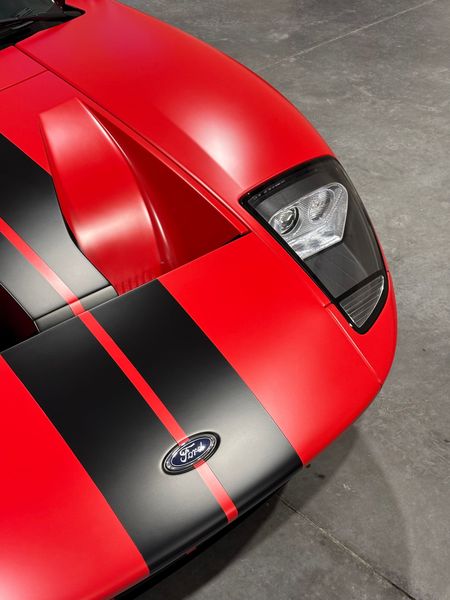 Red Ford GT with black racing stripes, a black headlight, and the Ford emblem, parked indoors.