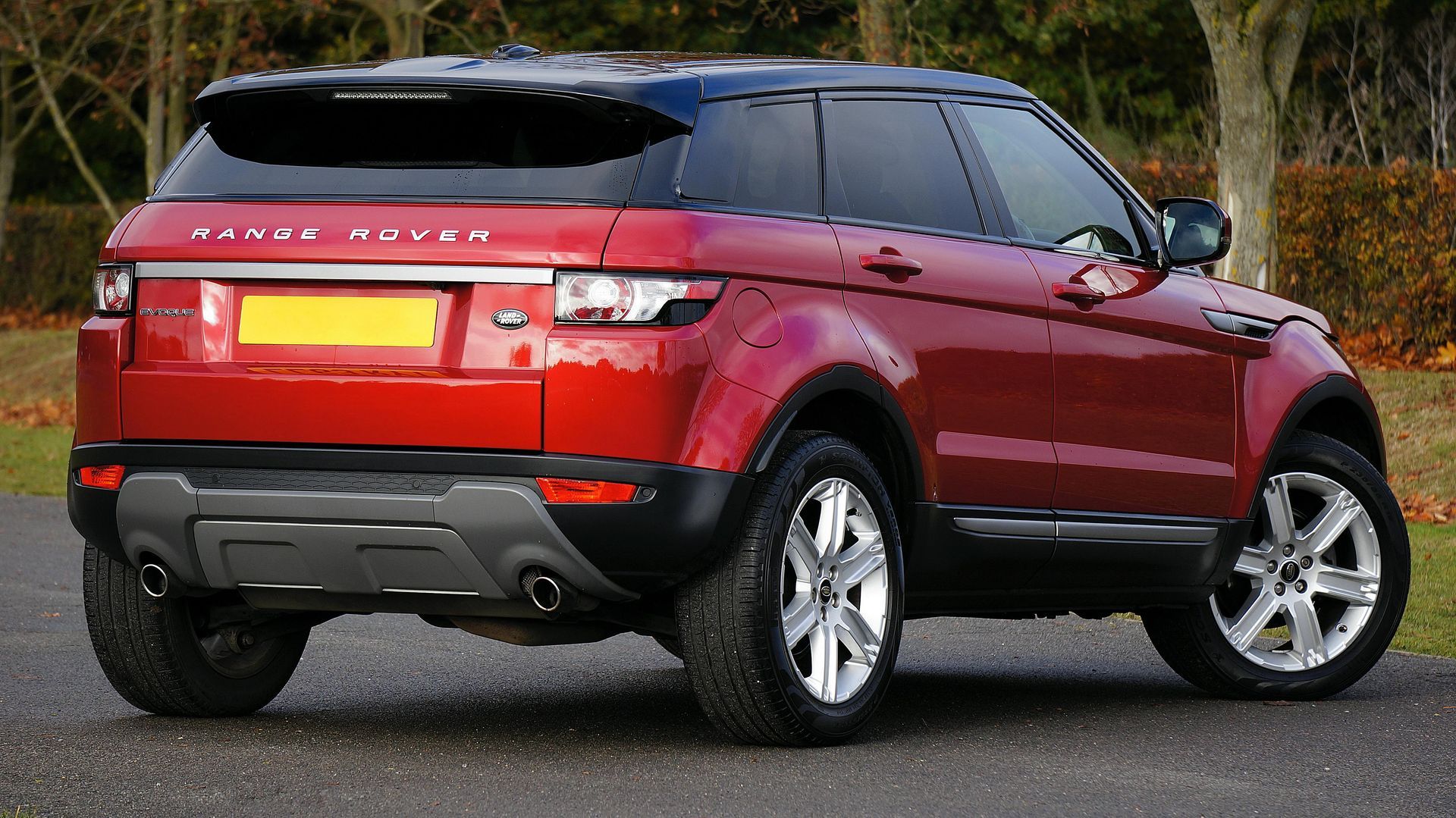 Red Range Rover SUV parked on asphalt, black roof, silver wheels, backyard setting.